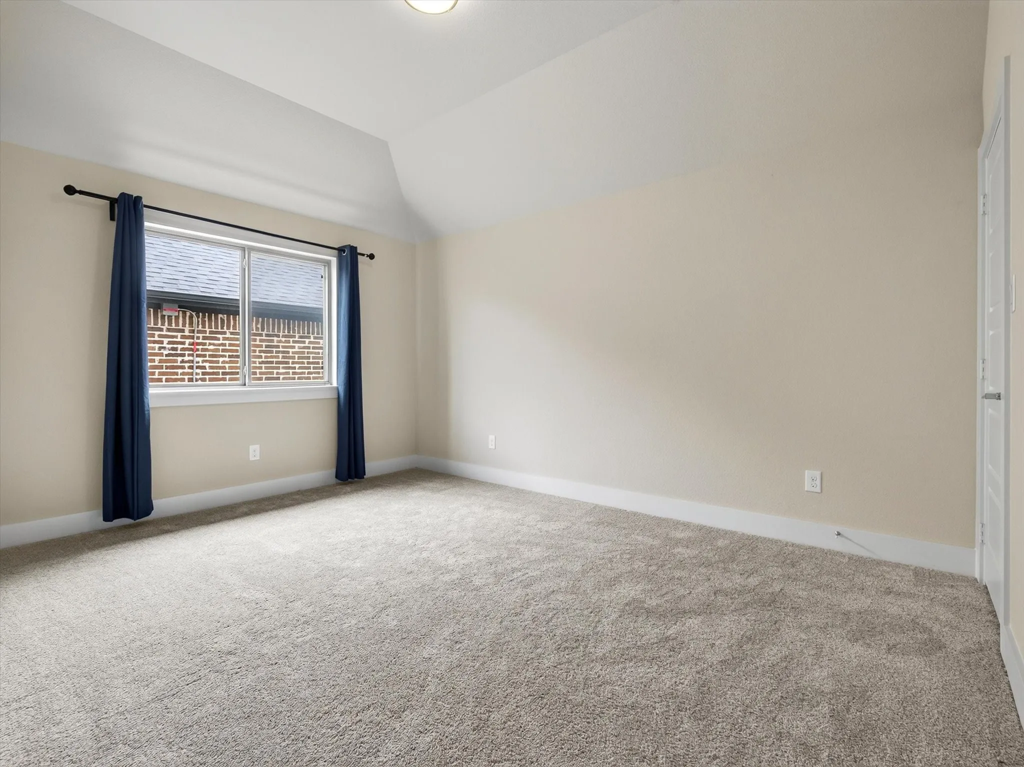 Spacious room featuring vaulted ceilings, neutral-toned walls, and plush carpeting