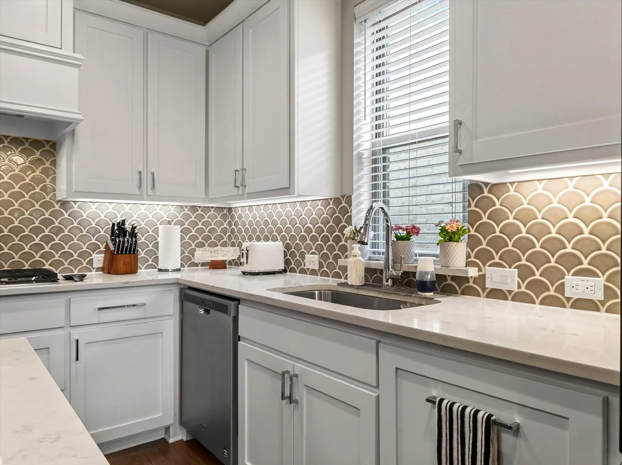 Kitchen featuring white shaker-style cabinetry, light-toned countertops, and a decorative scallop-patterned backsplash