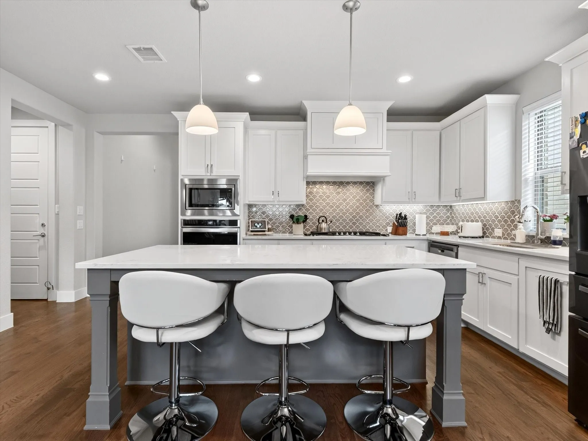 Kitchen featuring a central island with a light-toned countertop, pendant lighting, shaker-style cabinetry, stainless steel appliances, and wood-finish flooring