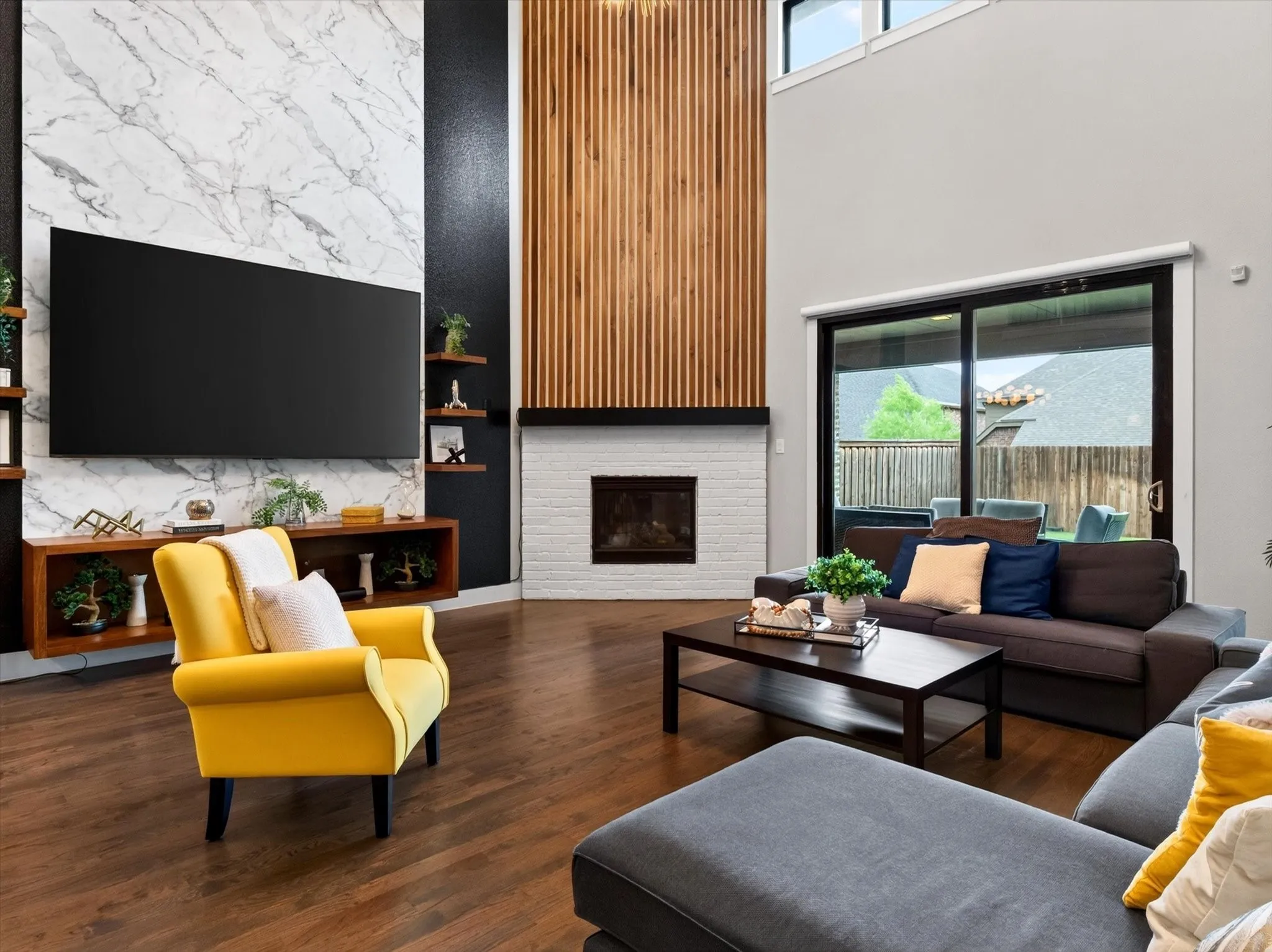 Living room featuring a two-story ceiling, wood-finish flooring, and a fireplace with a white brick surround