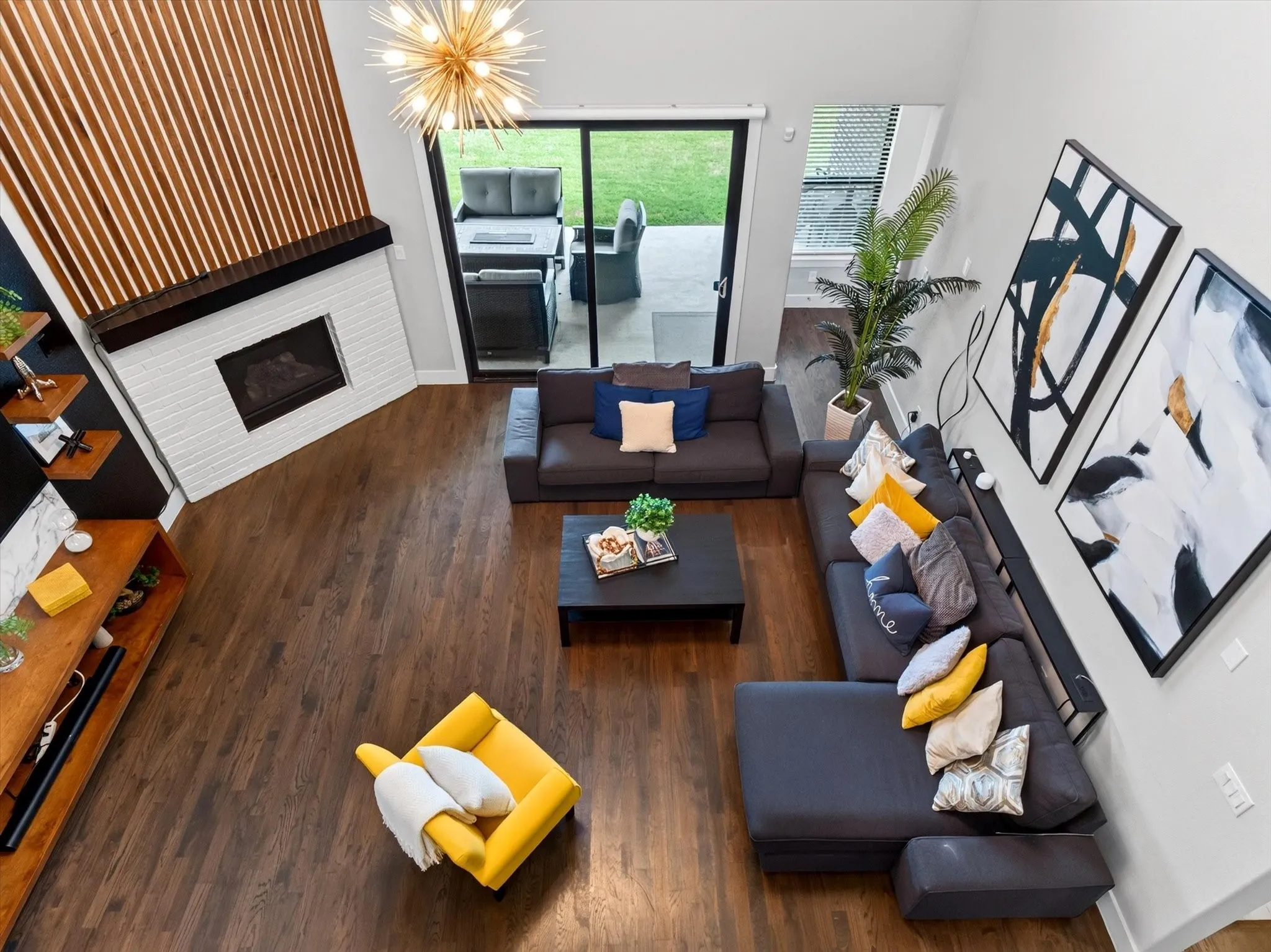 Spacious living area featuring wood-finish flooring, a white brick fireplace with a dark mantel, and a striking vertical wood slat accent wall