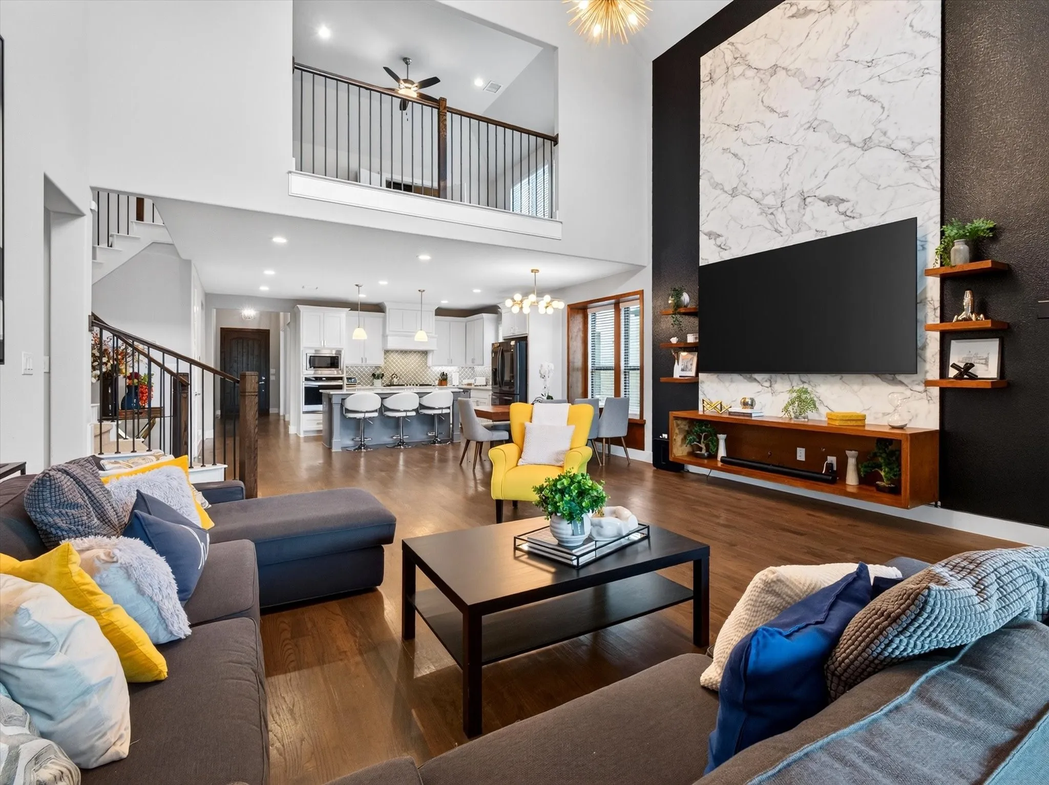 Spacious open-concept living area featuring high ceilings, wood-finish flooring, and a contemporary media wall with marble-look paneling