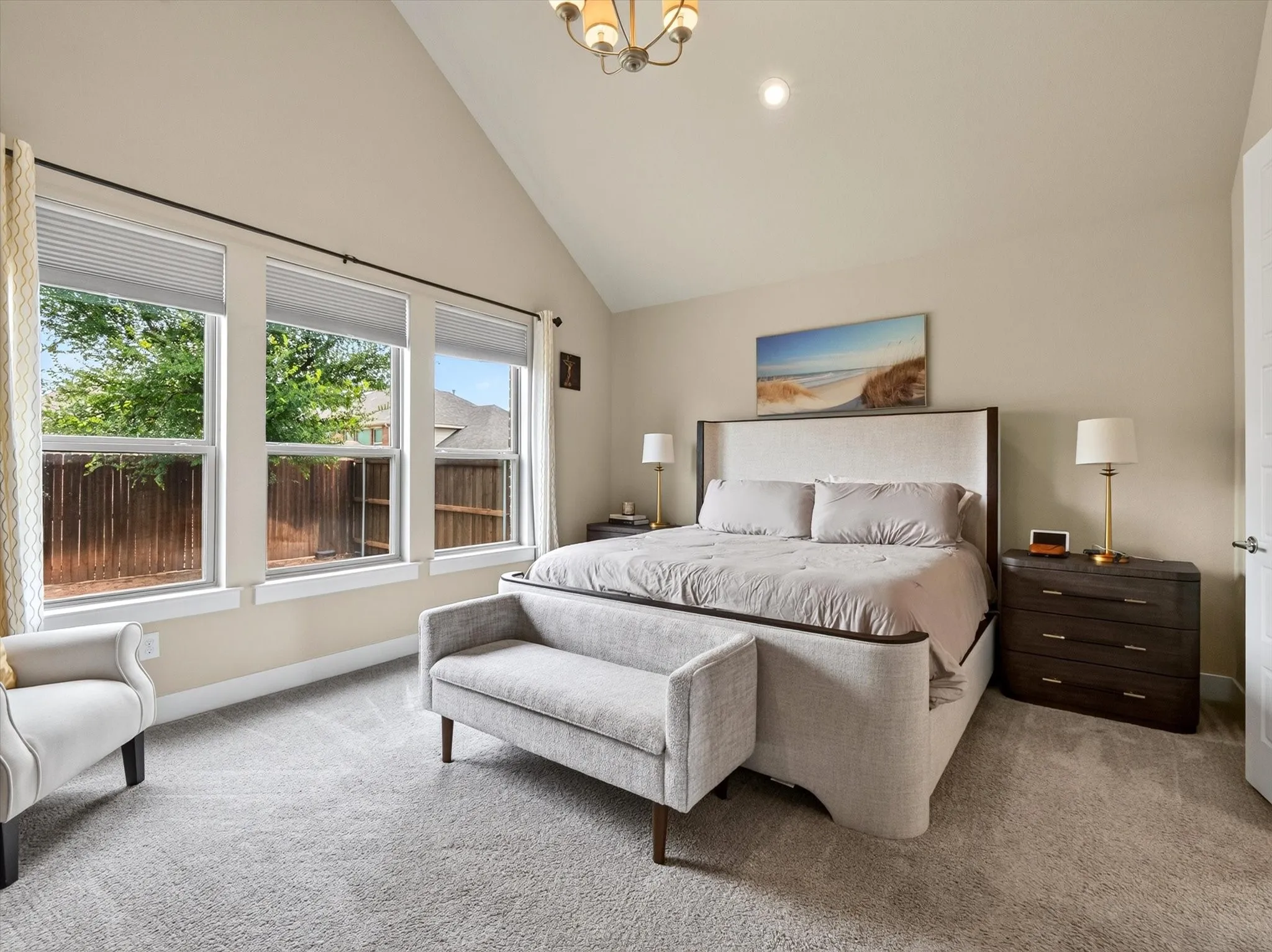 Vaulted ceiling bedroom with three large windows providing abundant natural light, light-toned carpeting, and neutral wall paint