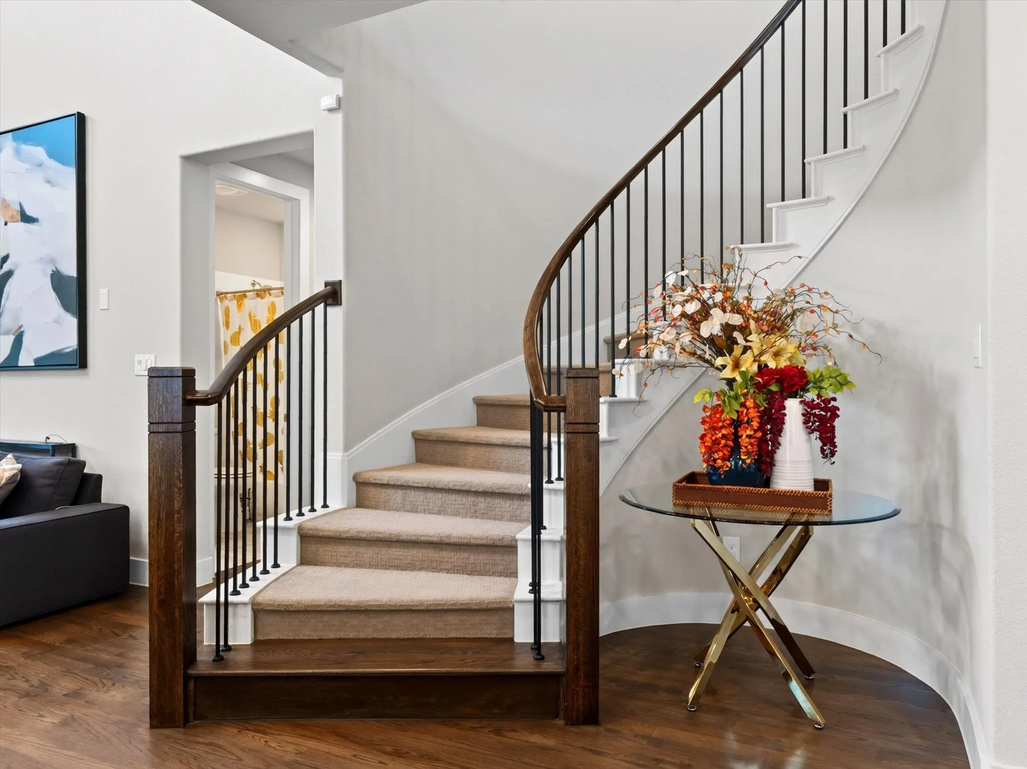 Curved staircase featuring dark wood handrails, black iron balusters, and carpeted treads