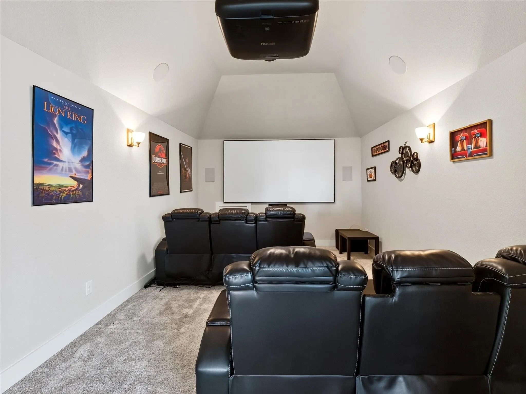 Dedicated media room featuring a vaulted ceiling and wall-mounted sconce lighting