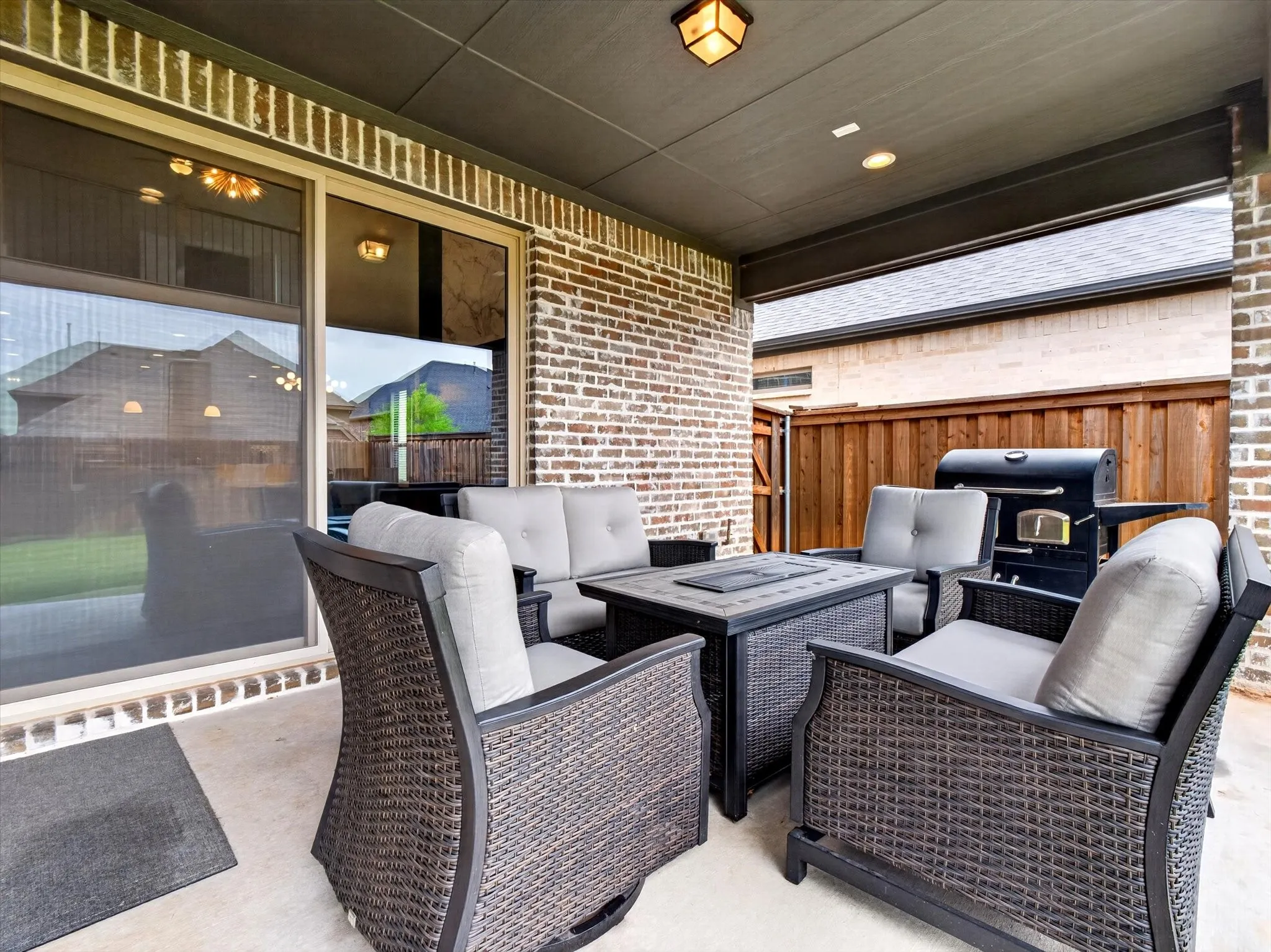 Covered patio featuring a brick exterior wall, concrete flooring, sliding glass doors, and a wood privacy fence