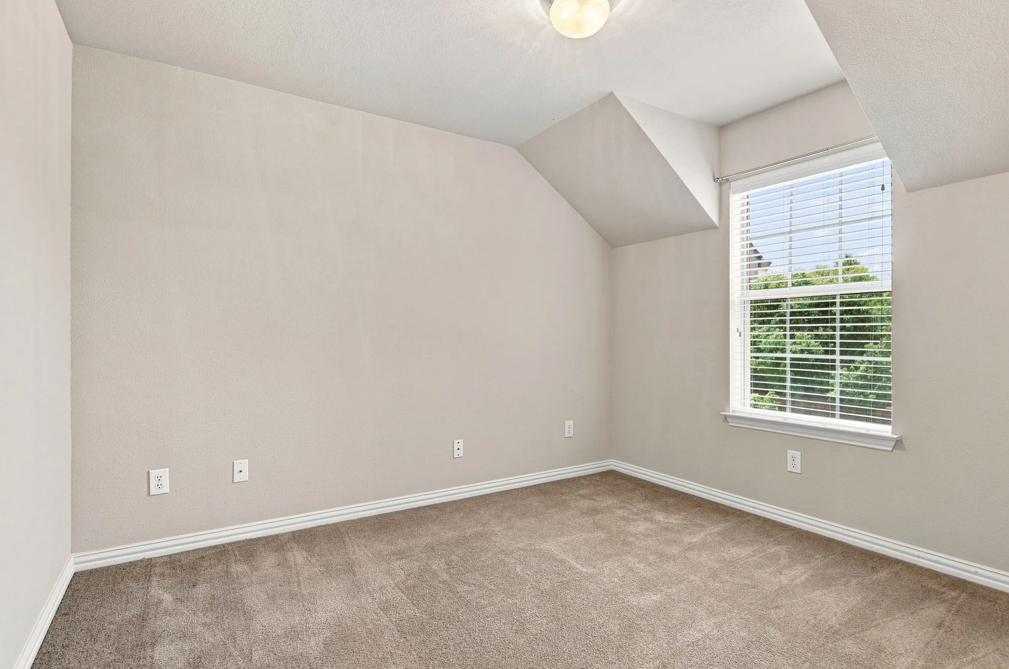 Neutral tone walls, sloped ceiling detail, large window with blinds, baseboard trim, and carpeted flooring