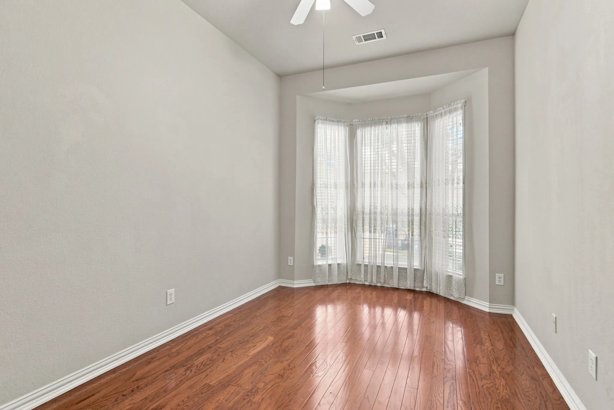 Bay window with multiple panels, wood-finish flooring, and a ceiling fan