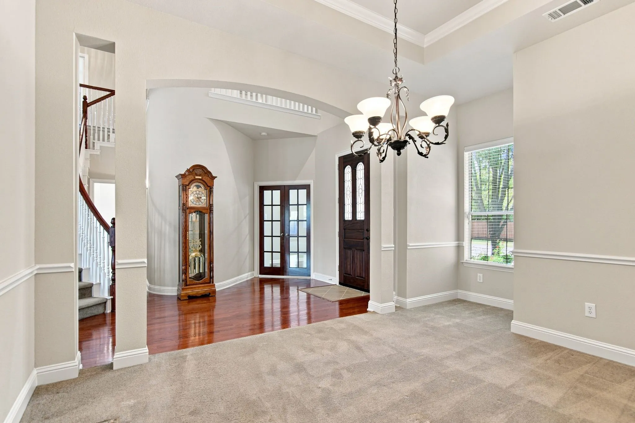 Tray ceiling with a decorative chandelier, dual paneled entry doors, and wood-finish flooring