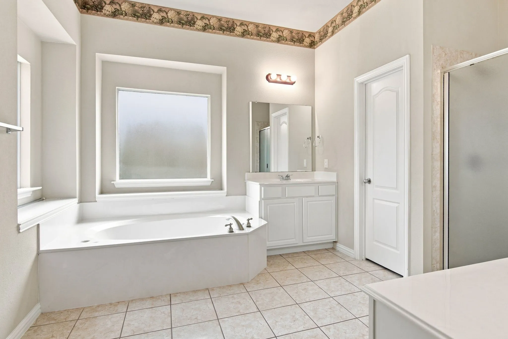 Soaking tub with frosted window, white vanity with integrated sink, glass-enclosed shower, and tile flooring