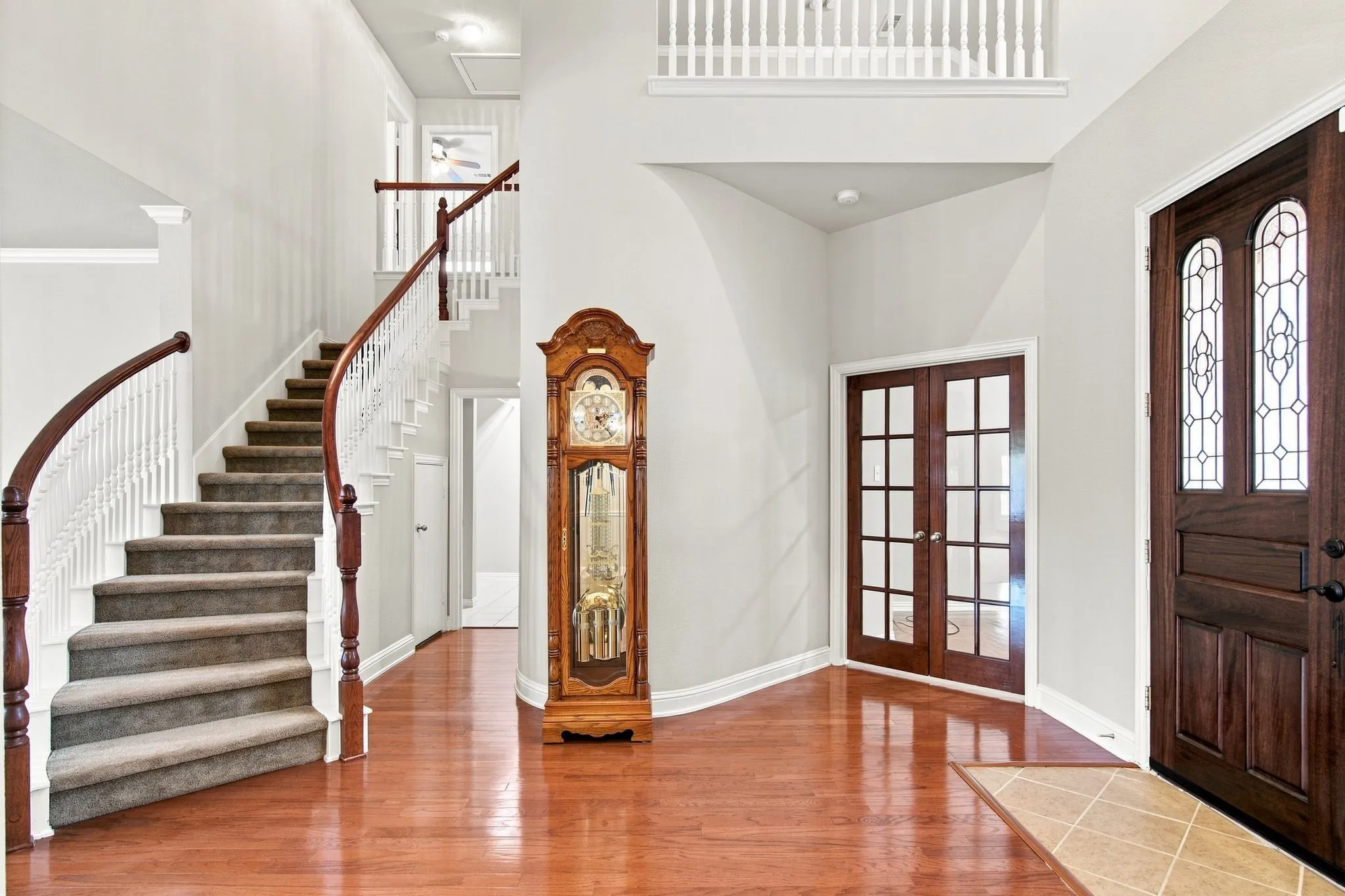 Hardwood flooring, curved staircase with carpeted treads, French doors, leaded glass entry door, and a second-story landing with white balusters