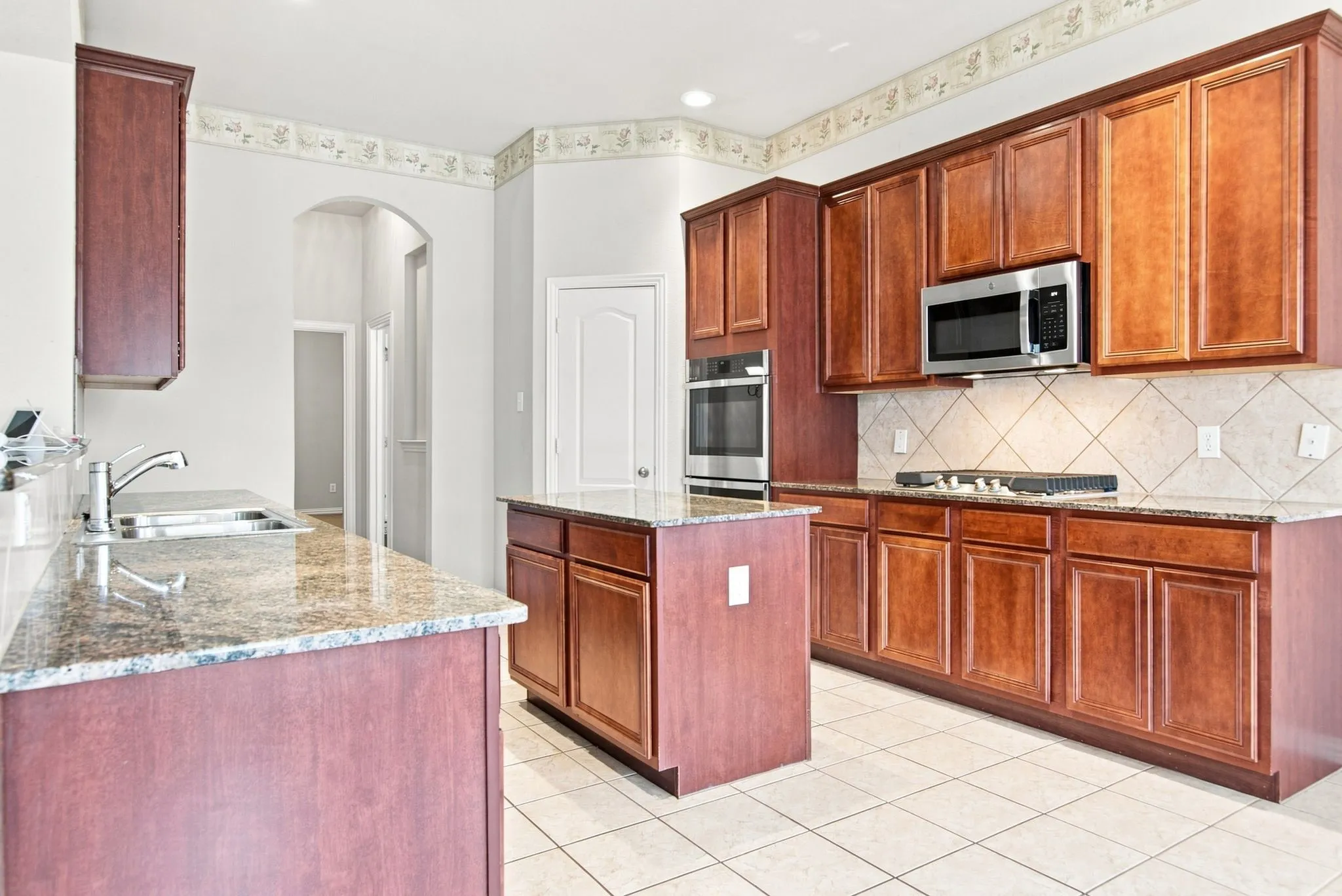 Kitchen featuring wood-finish cabinetry, granite countertops, stainless steel appliances, tile flooring, and a center island
