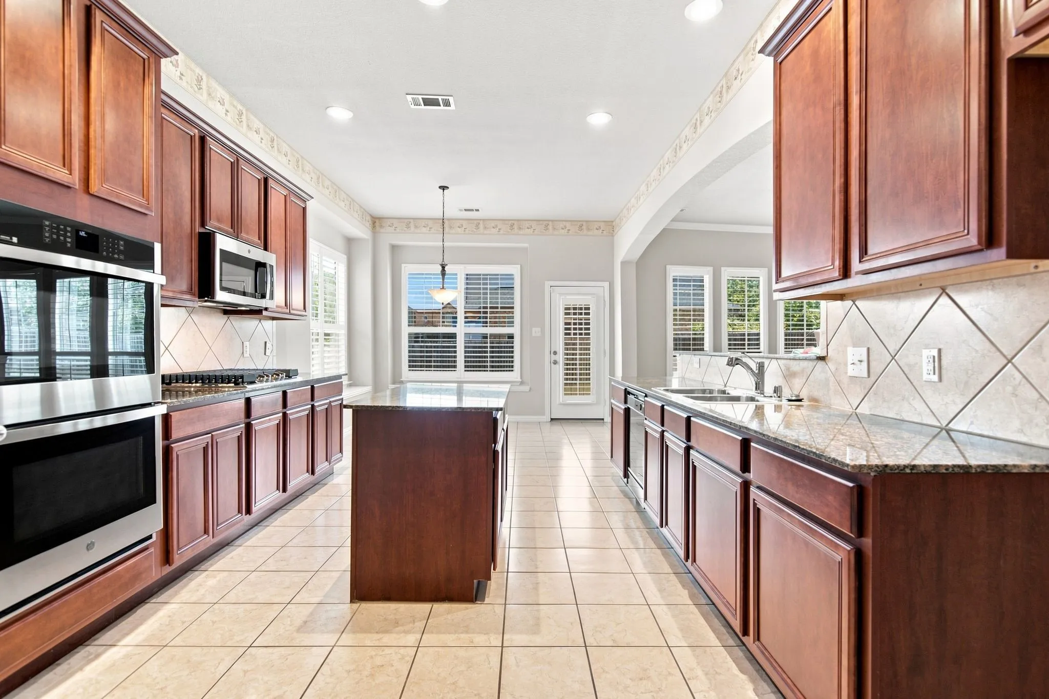 Kitchen featuring extensive wood cabinetry, tile flooring, central island, stainless steel built-in double oven, and stainless steel microwave