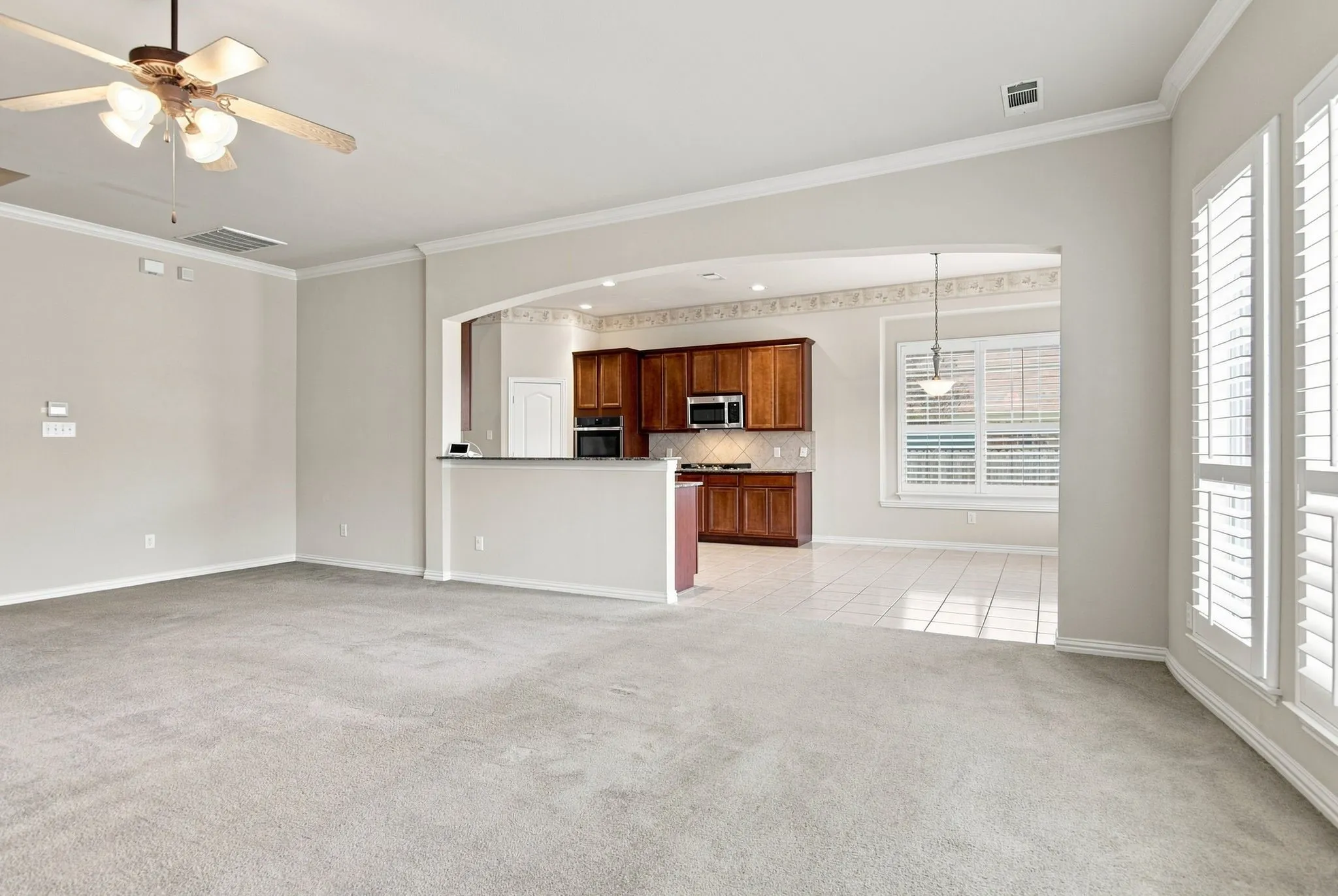 Carpeted living area with a ceiling fan, crown molding, and plantation shutters