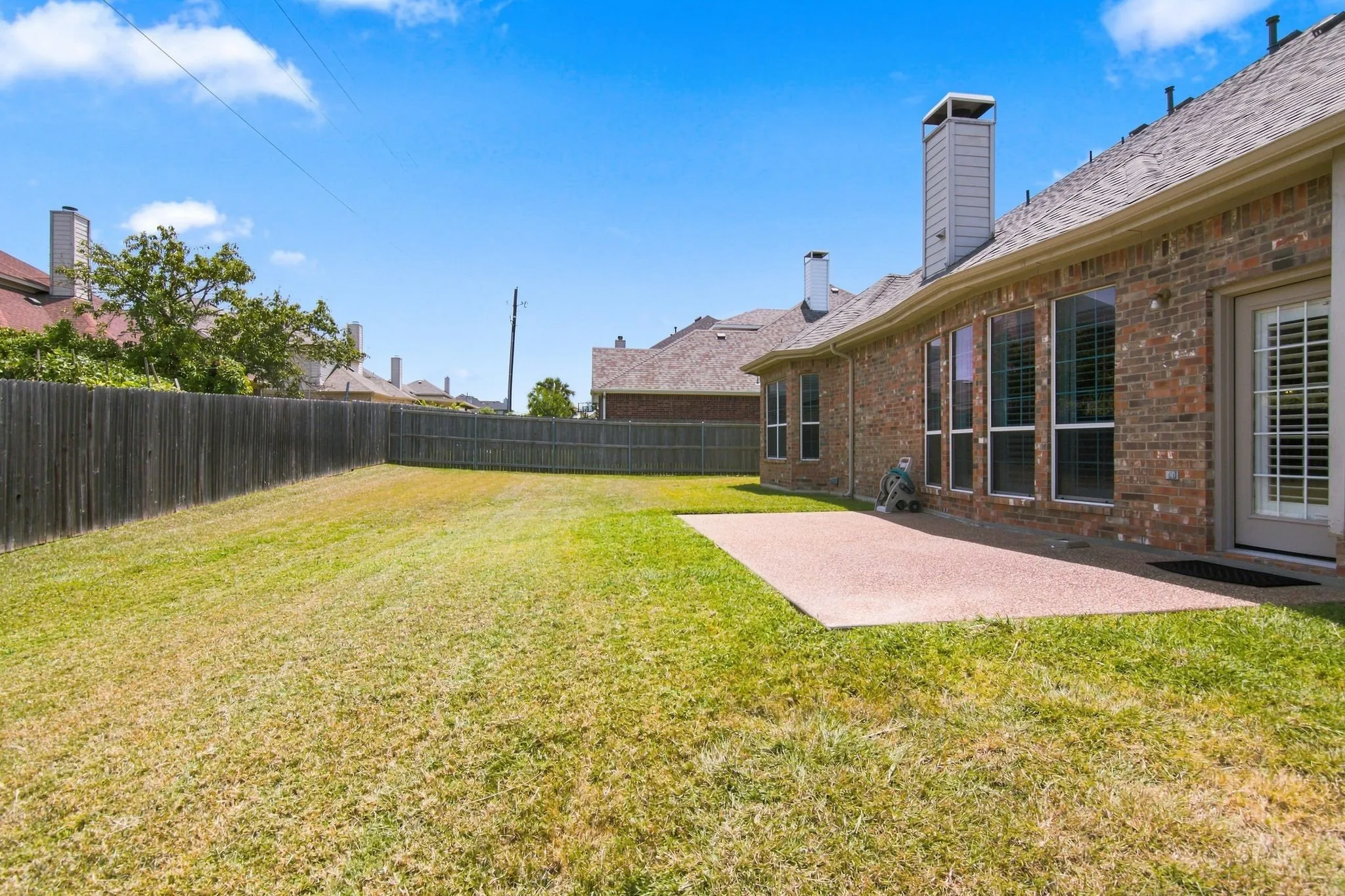 Expansive backyard featuring a manicured lawn, full privacy fencing, and a concrete patio