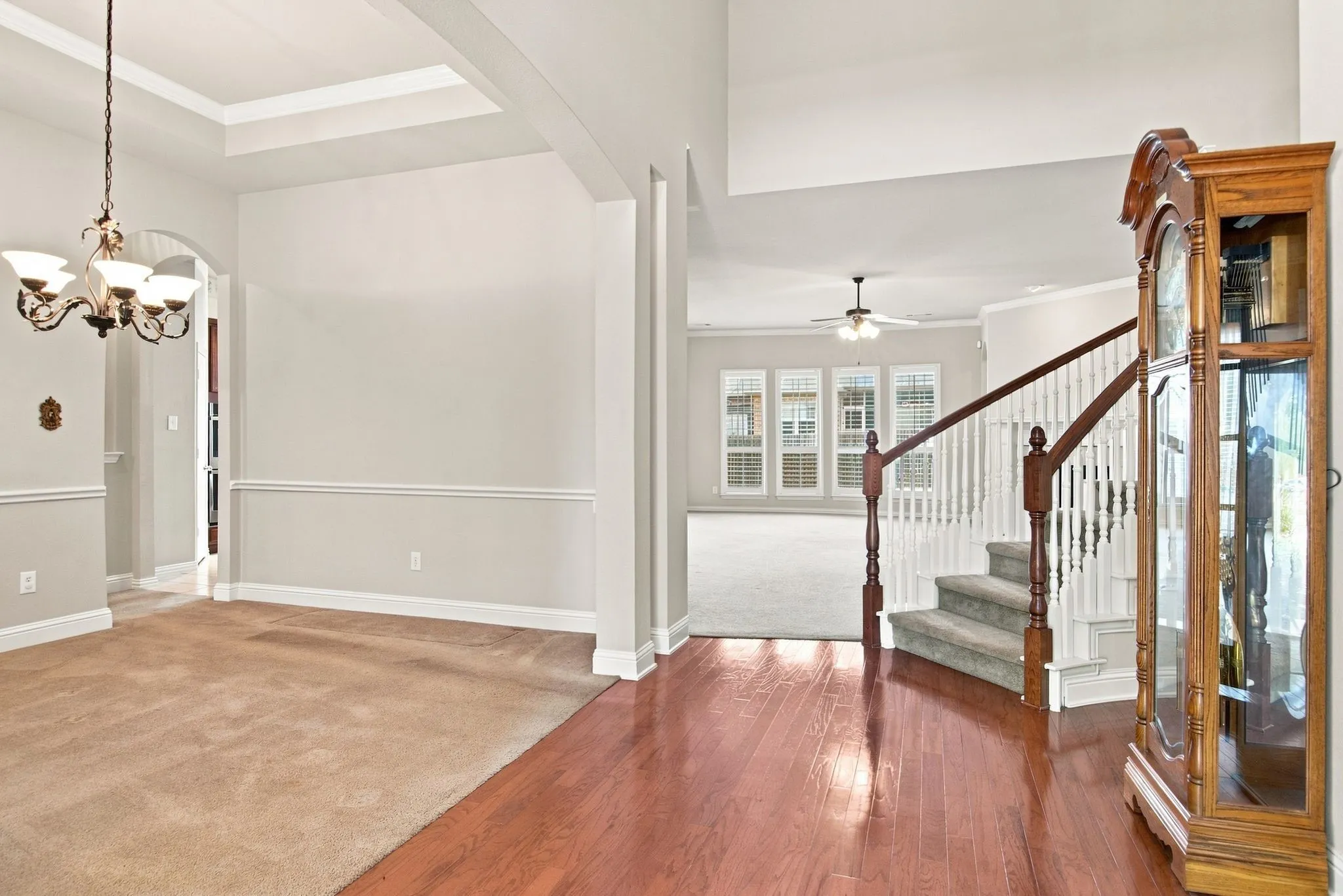 Hardwood flooring, tray ceiling, chandelier, carpeted stairs, and a multi-pane window
