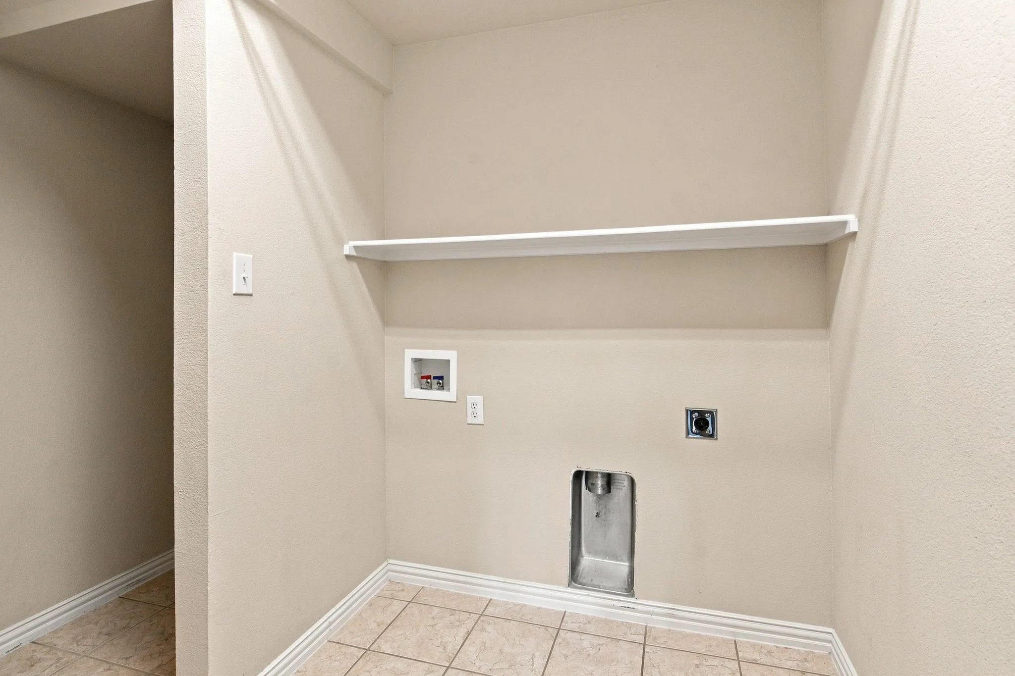 Dedicated utility space with a built-in shelf, neutral wall tones, and ceramic tile flooring