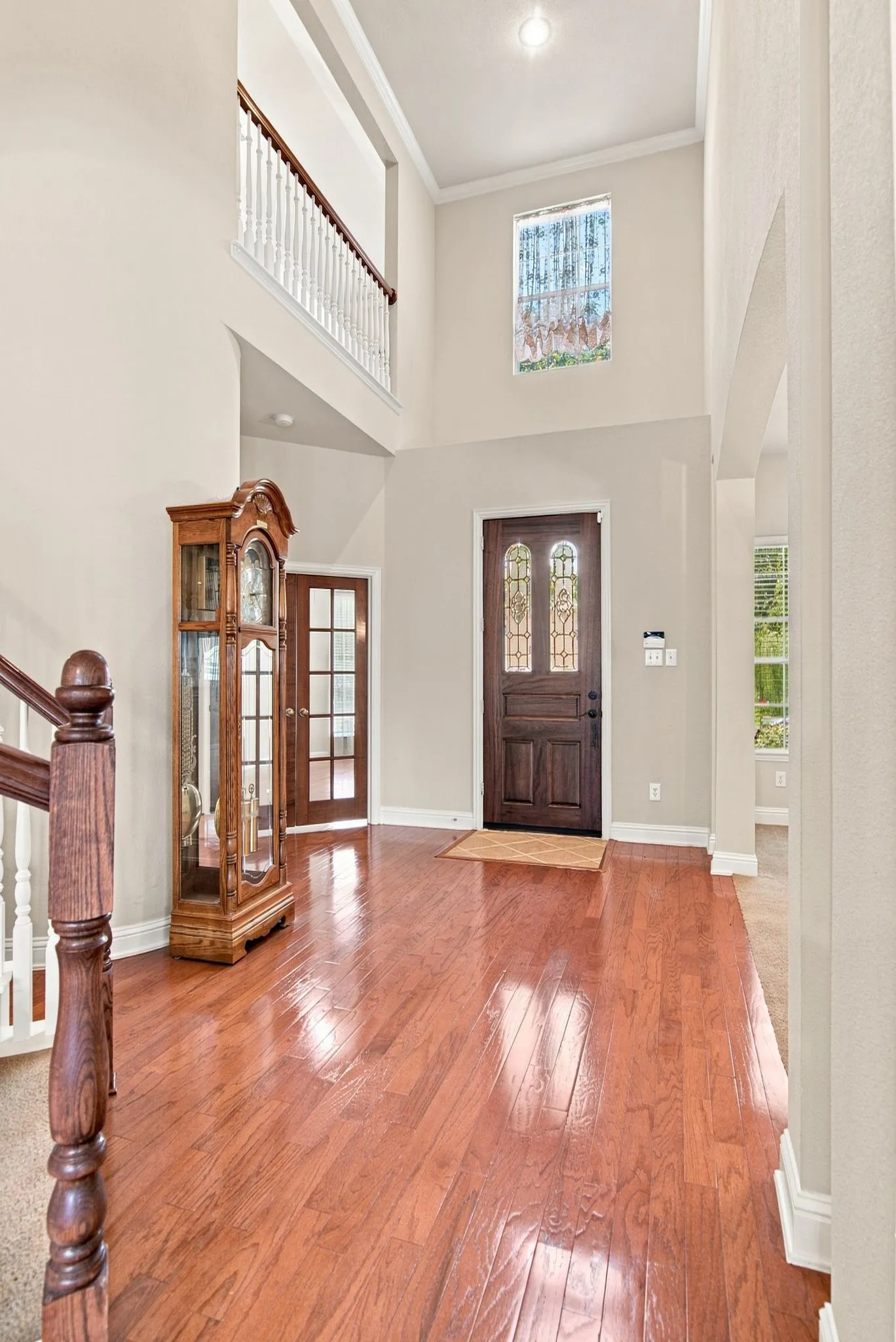 Two-story foyer with wood-finish flooring, a decorative transom window, and a dark wood entry door with leaded glass