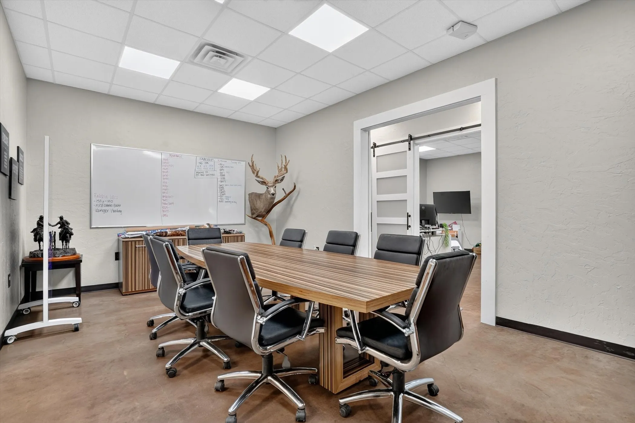 Conference room featuring a wood-finish table, polished concrete flooring, white walls, and a barn door entry with frosted glass panels