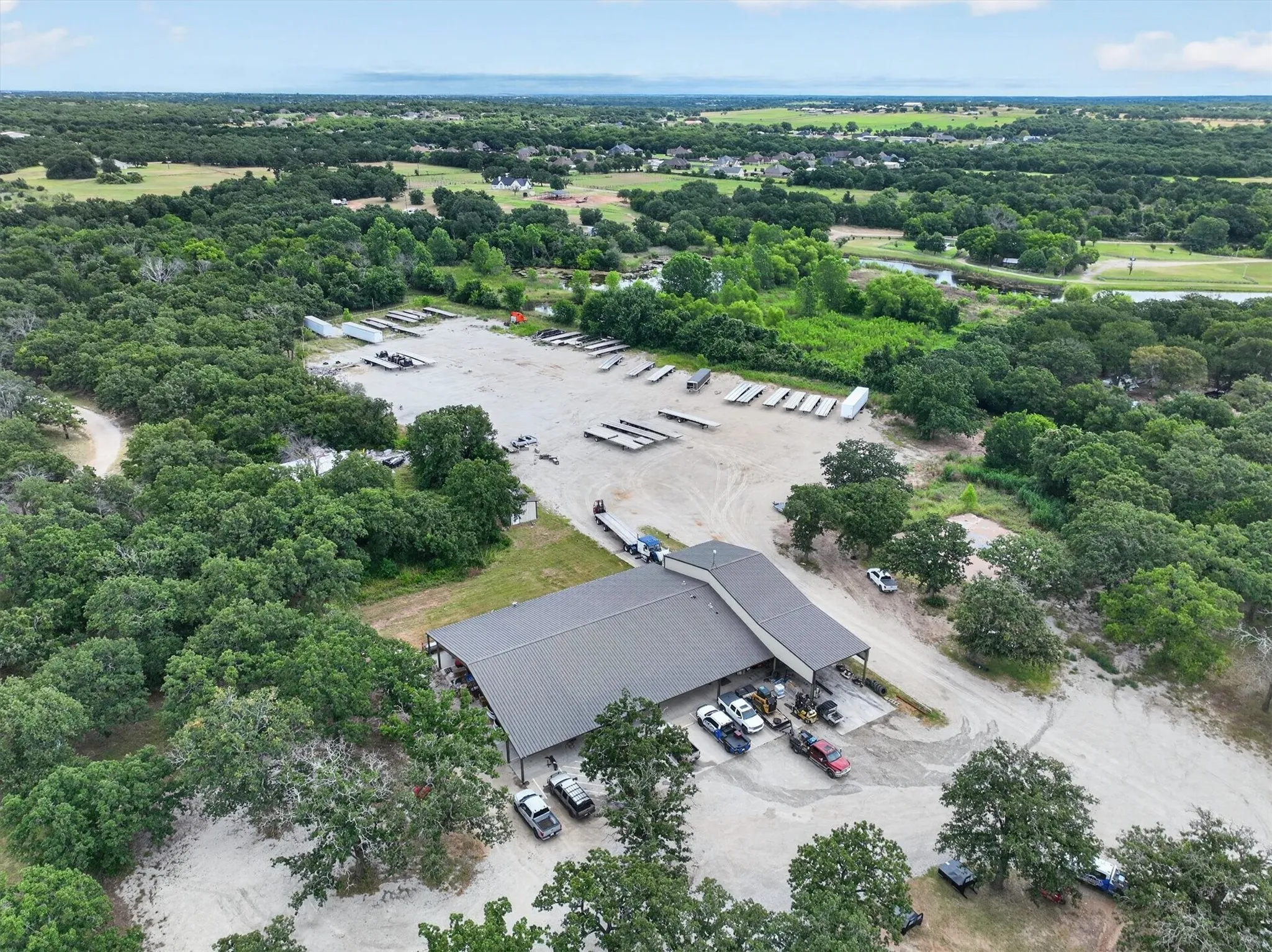Expansive commercial property featuring a large main building with a dark-pitched roof, surrounded by mature trees