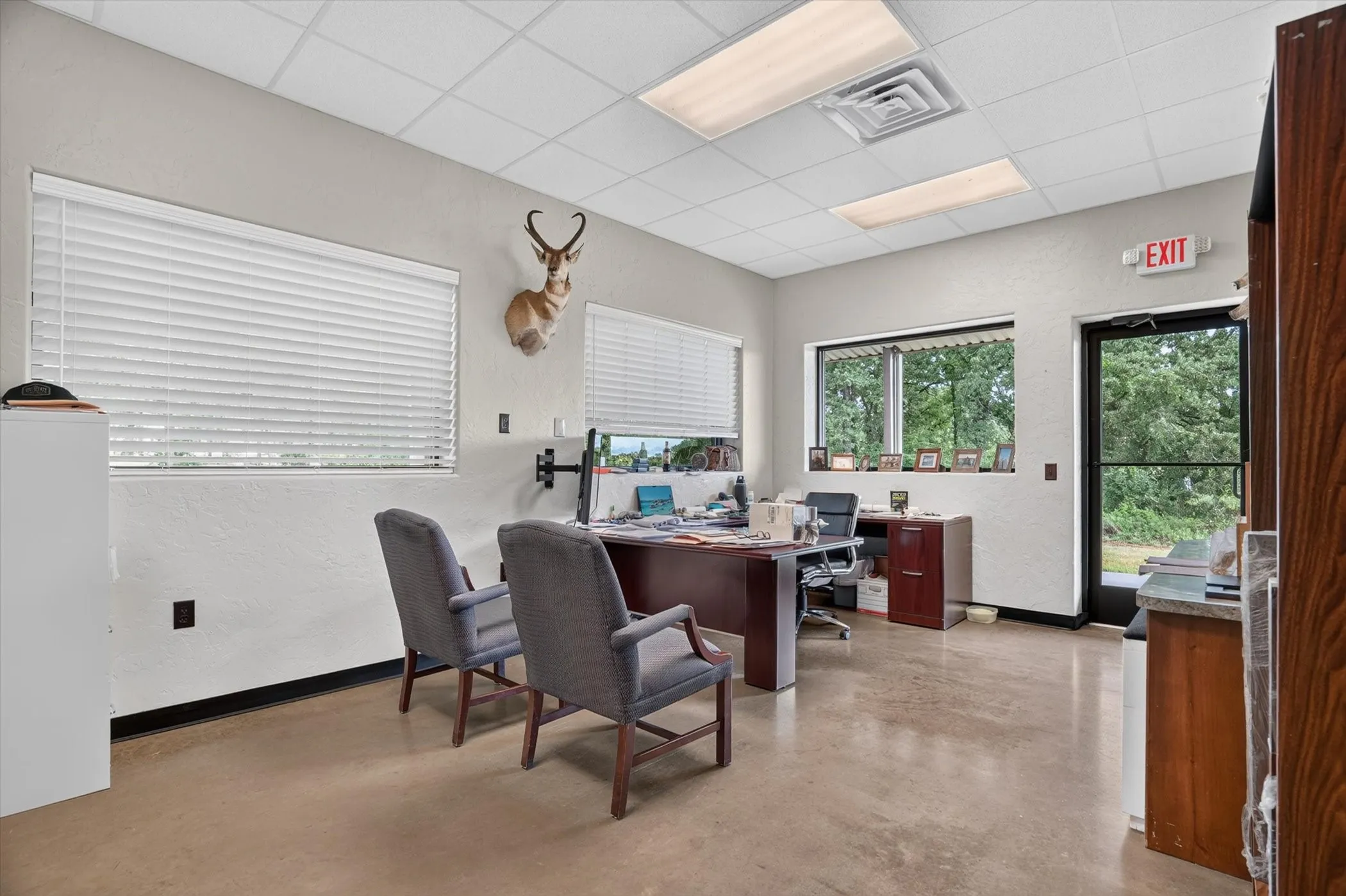 Spacious office area featuring light-toned walls, concrete flooring, and a drop ceiling with integrated lighting