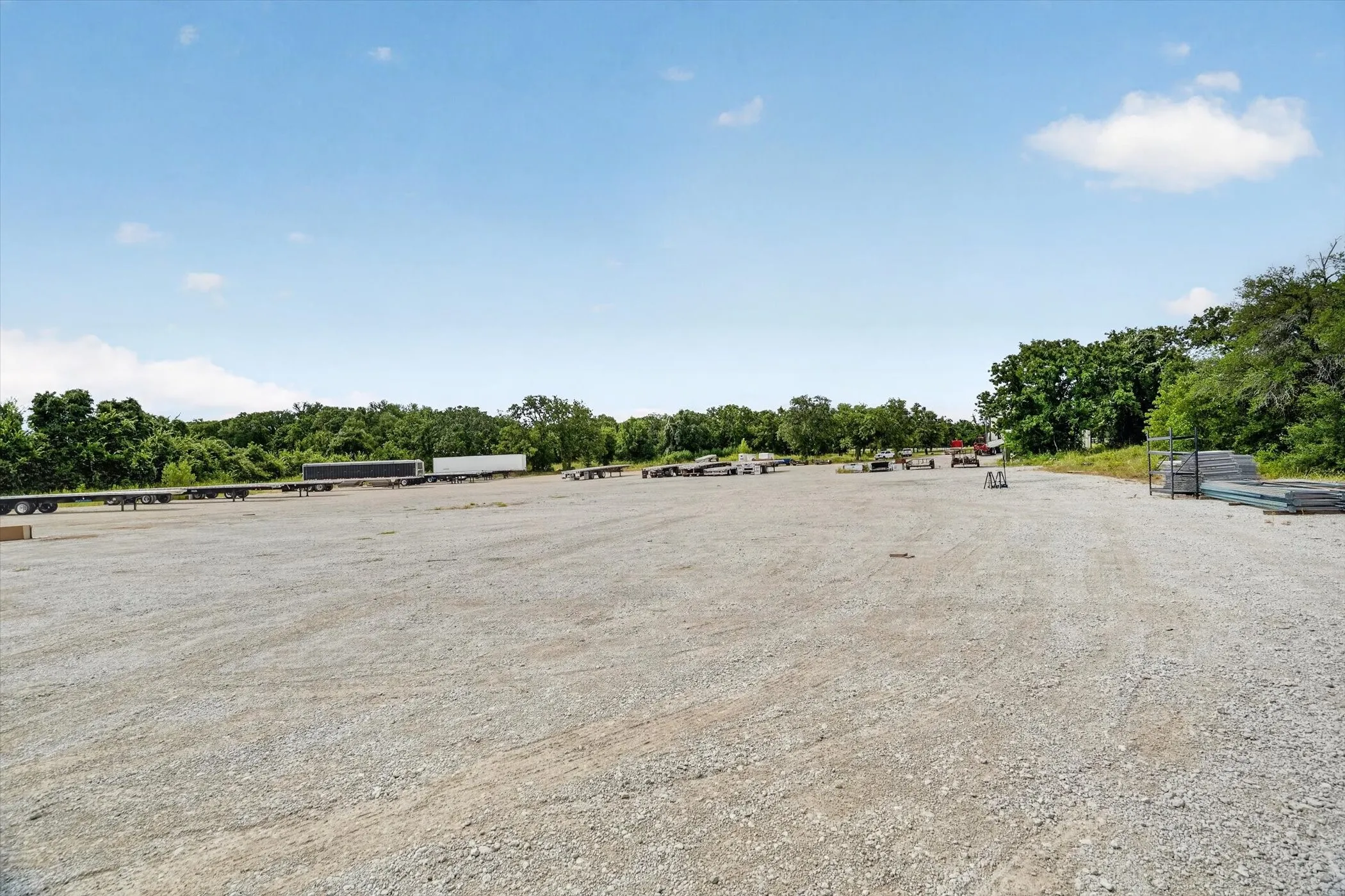 Expansive gravel lot with clear ground, bordered by mature trees