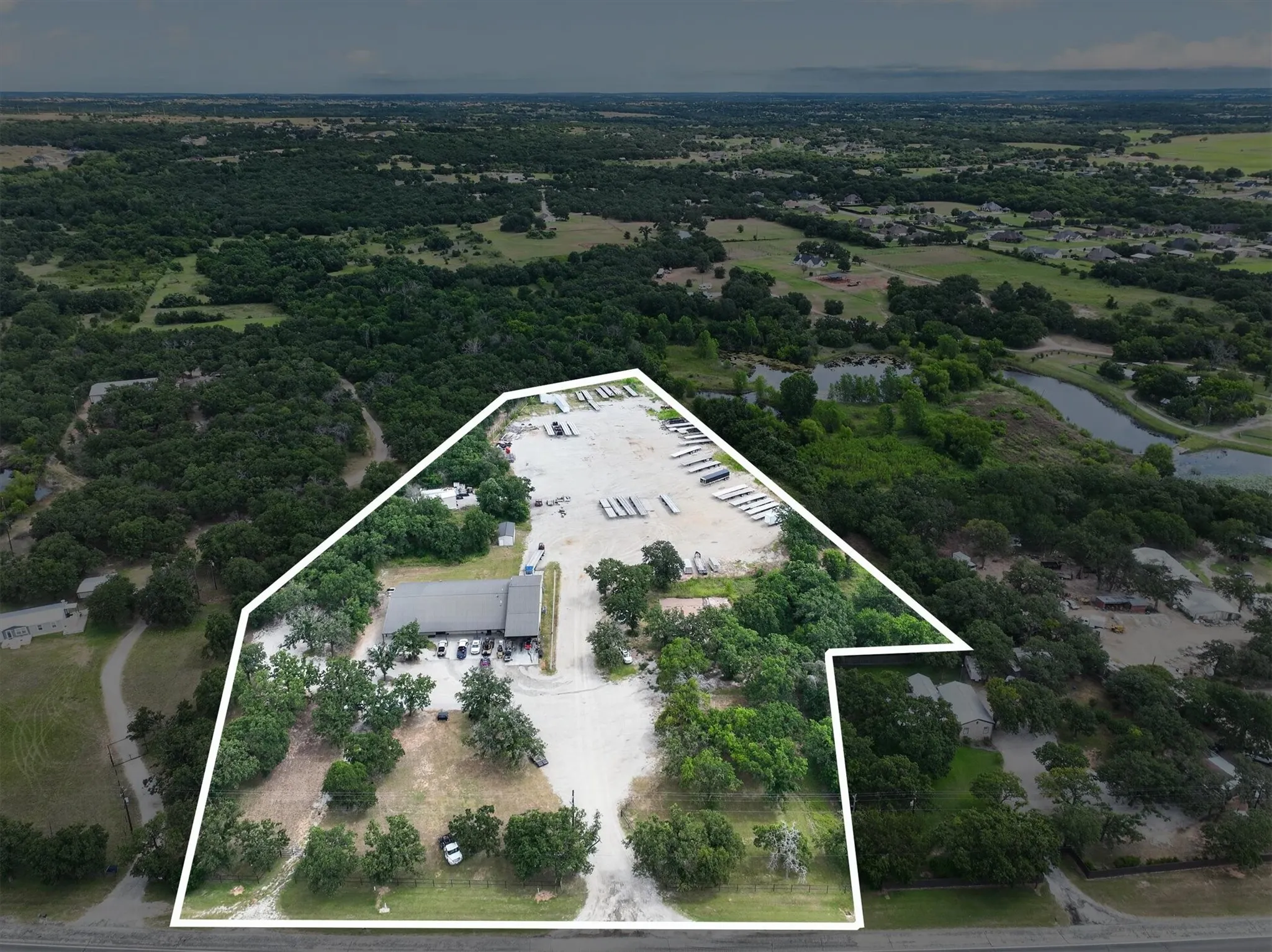 Expansive property featuring a commercial building with a dark-toned roof, a large gravel parking area, and a significant section of densely wooded land
