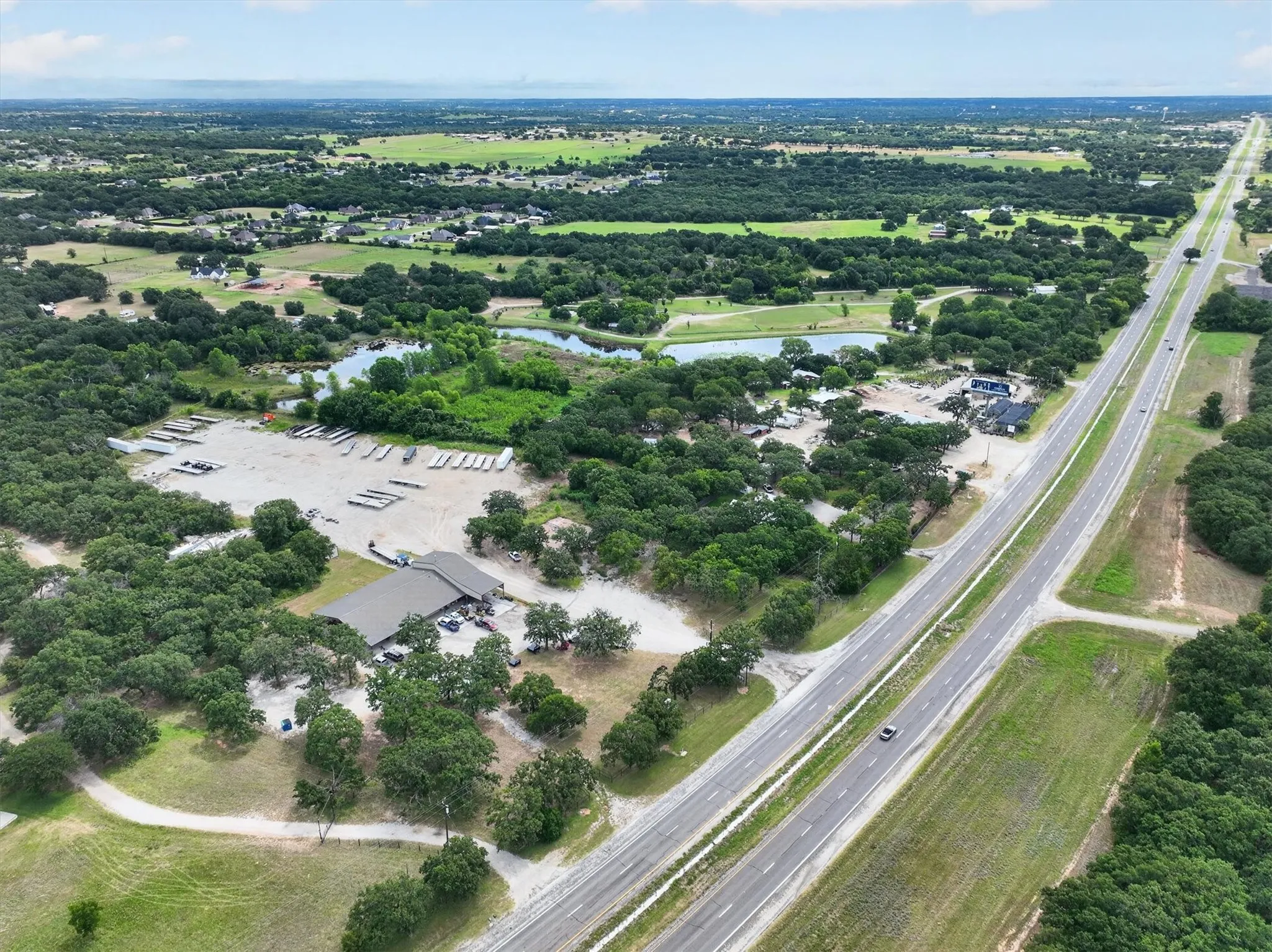 Expansive property with a commercial building and a large gravel lot for boats, bordered by mature trees and a pond