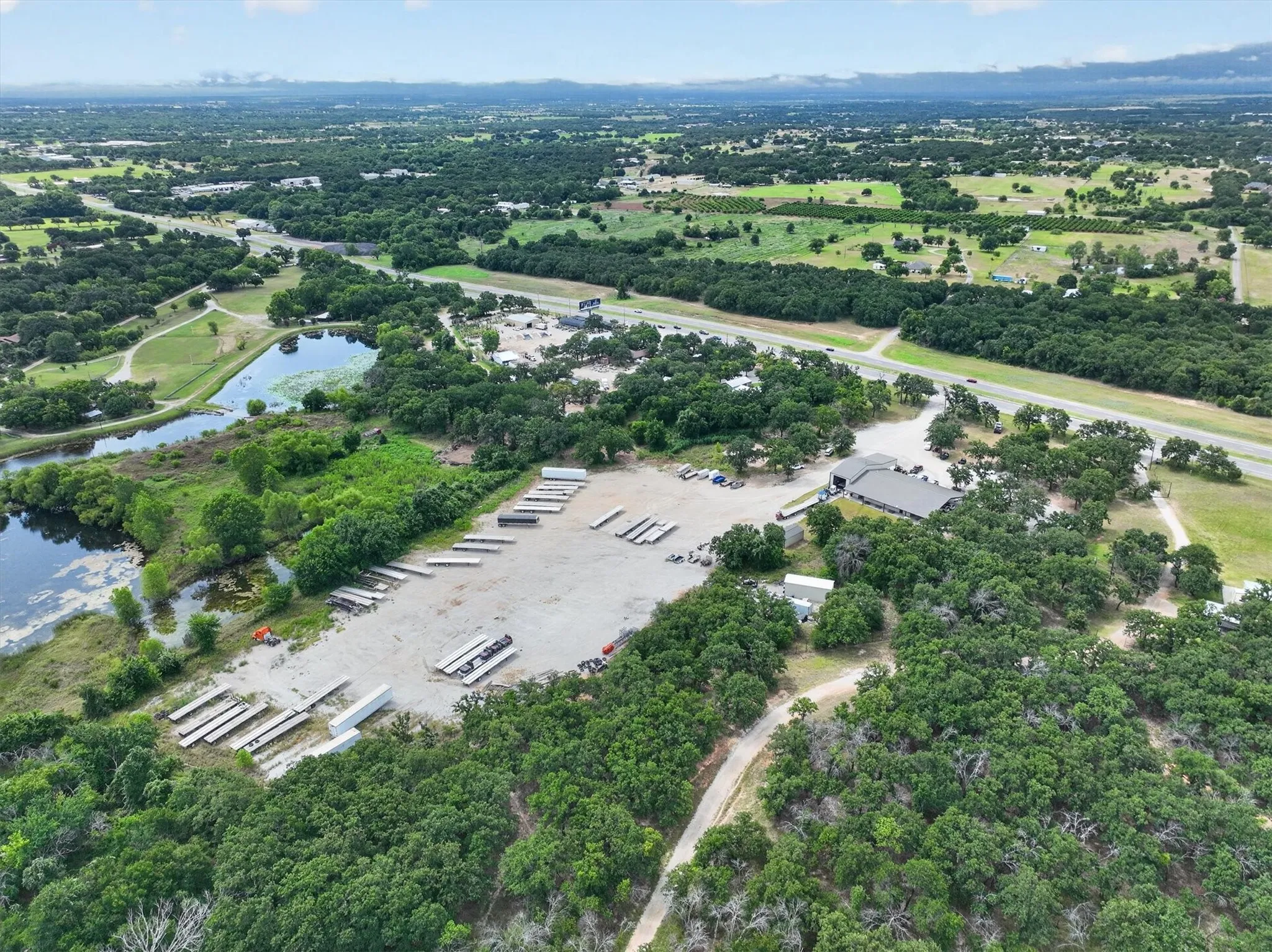 Expansive aerial perspective showcasing a commercial property with a paved lot, a large building with a dark roof, and direct access to a multi-lane highway