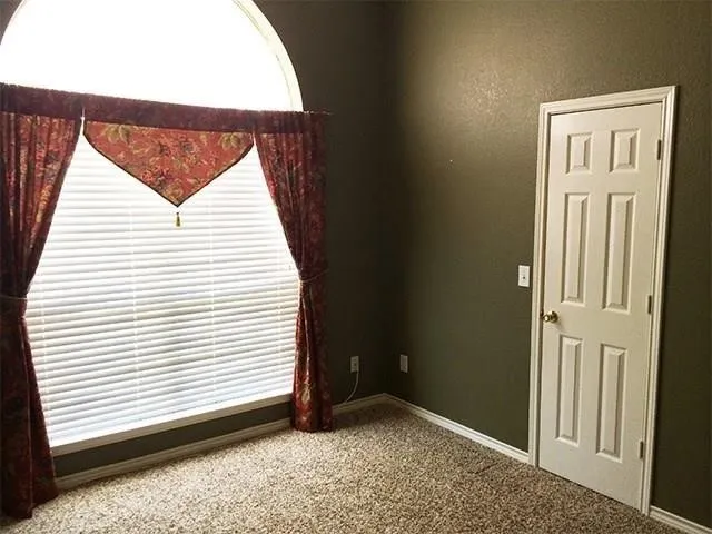 Room featuring an arched window with blinds, dark green painted walls, and textured carpet flooring