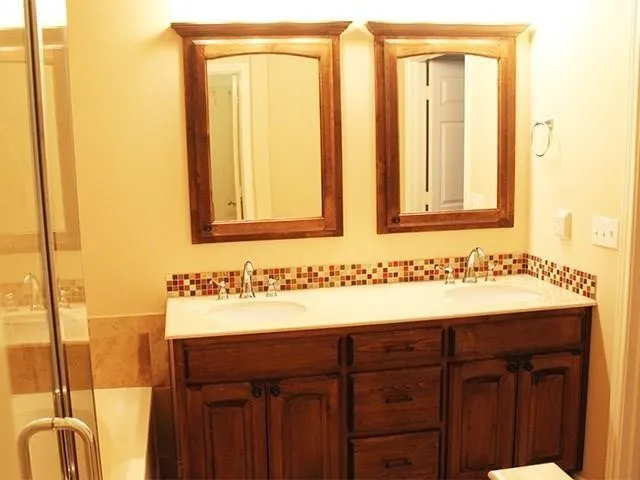 Double vanity featuring dark wood cabinetry, white countertops, dual undermount sinks, individual wood-framed mirrors, and mosaic tile backsplash