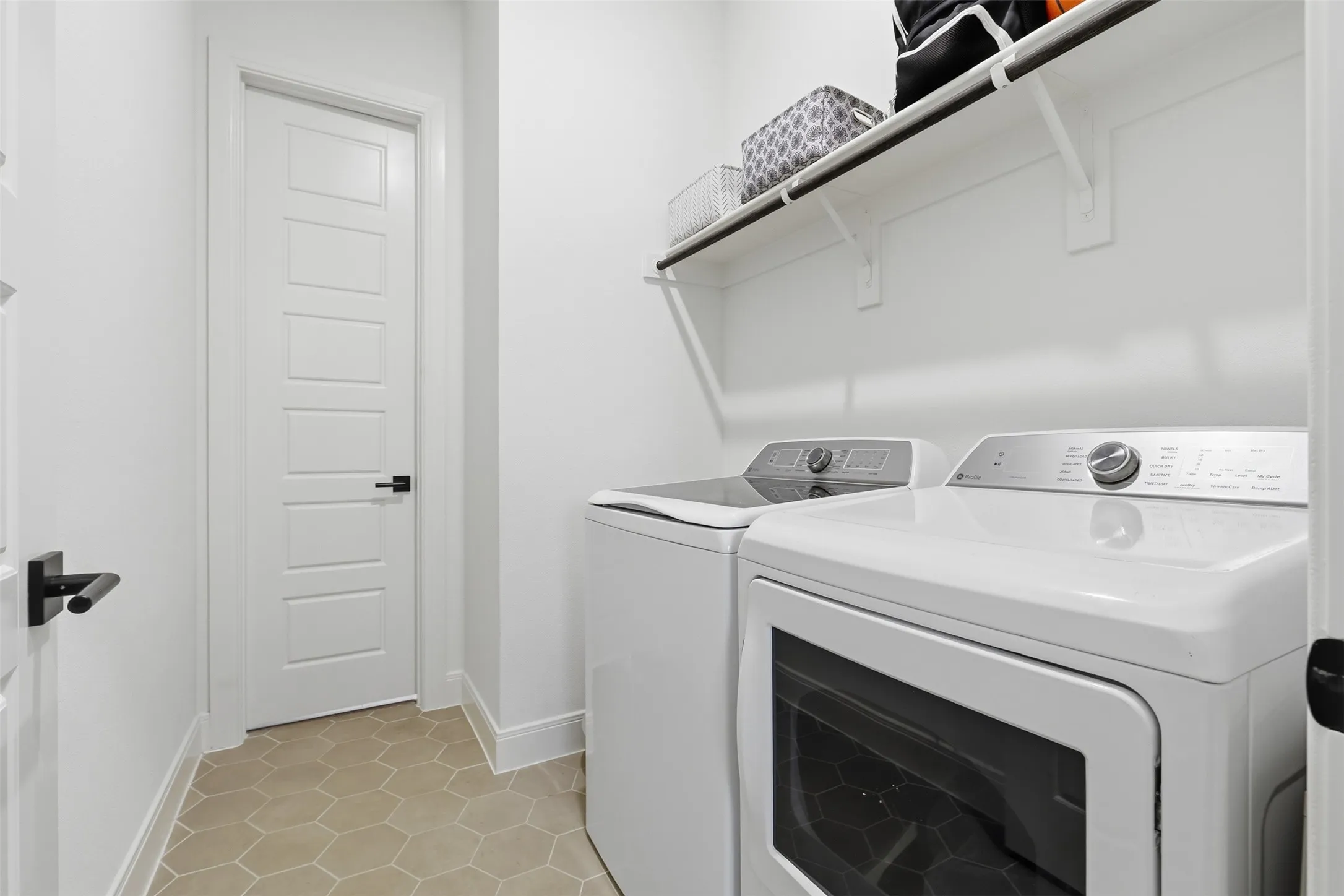 Dedicated utility space featuring hexagonal floor tiling, a white paneled door with black hardware, and built-in shelving