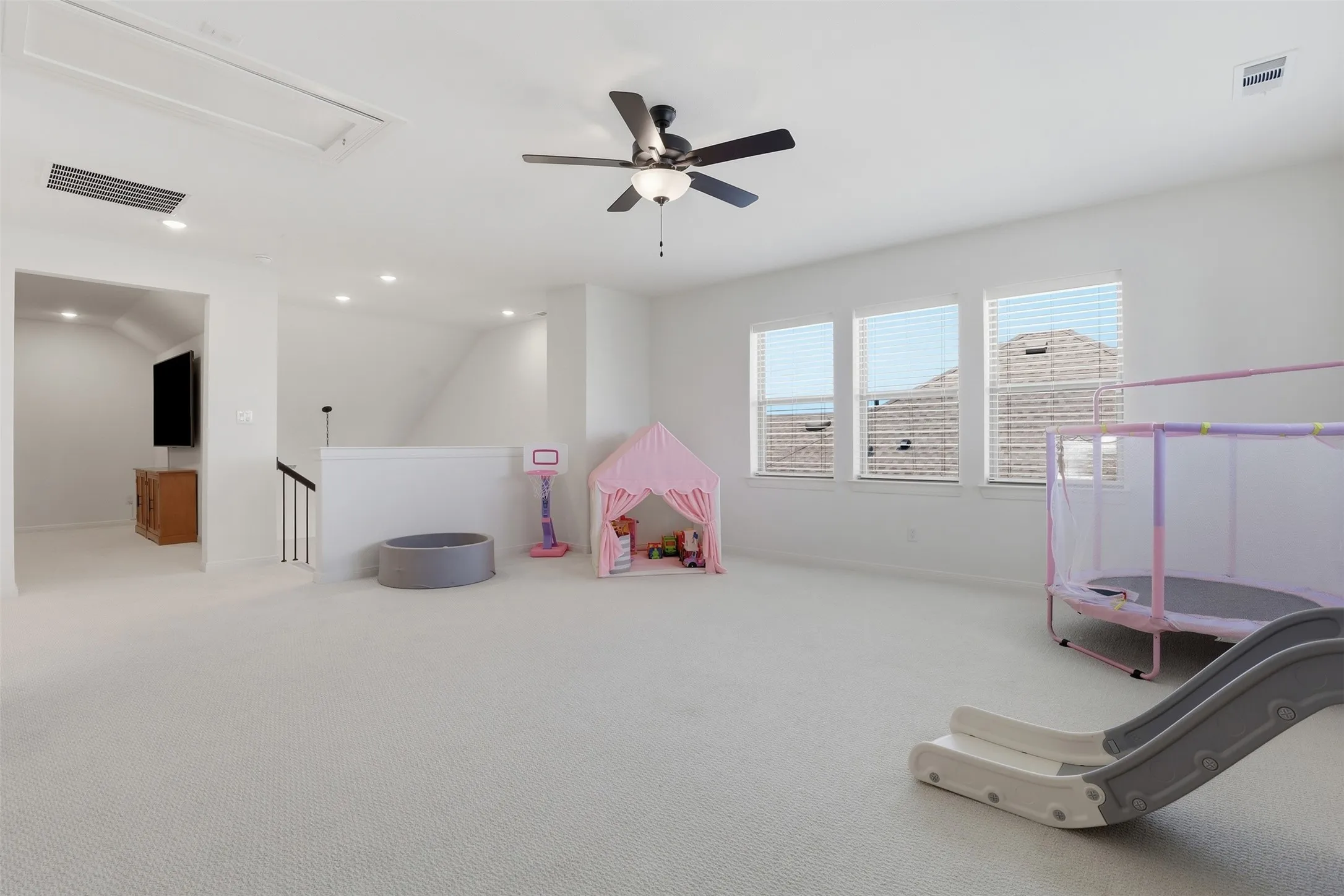 Spacious carpeted room featuring a ceiling fan with light fixture, multiple recessed lights, and three windows with blinds