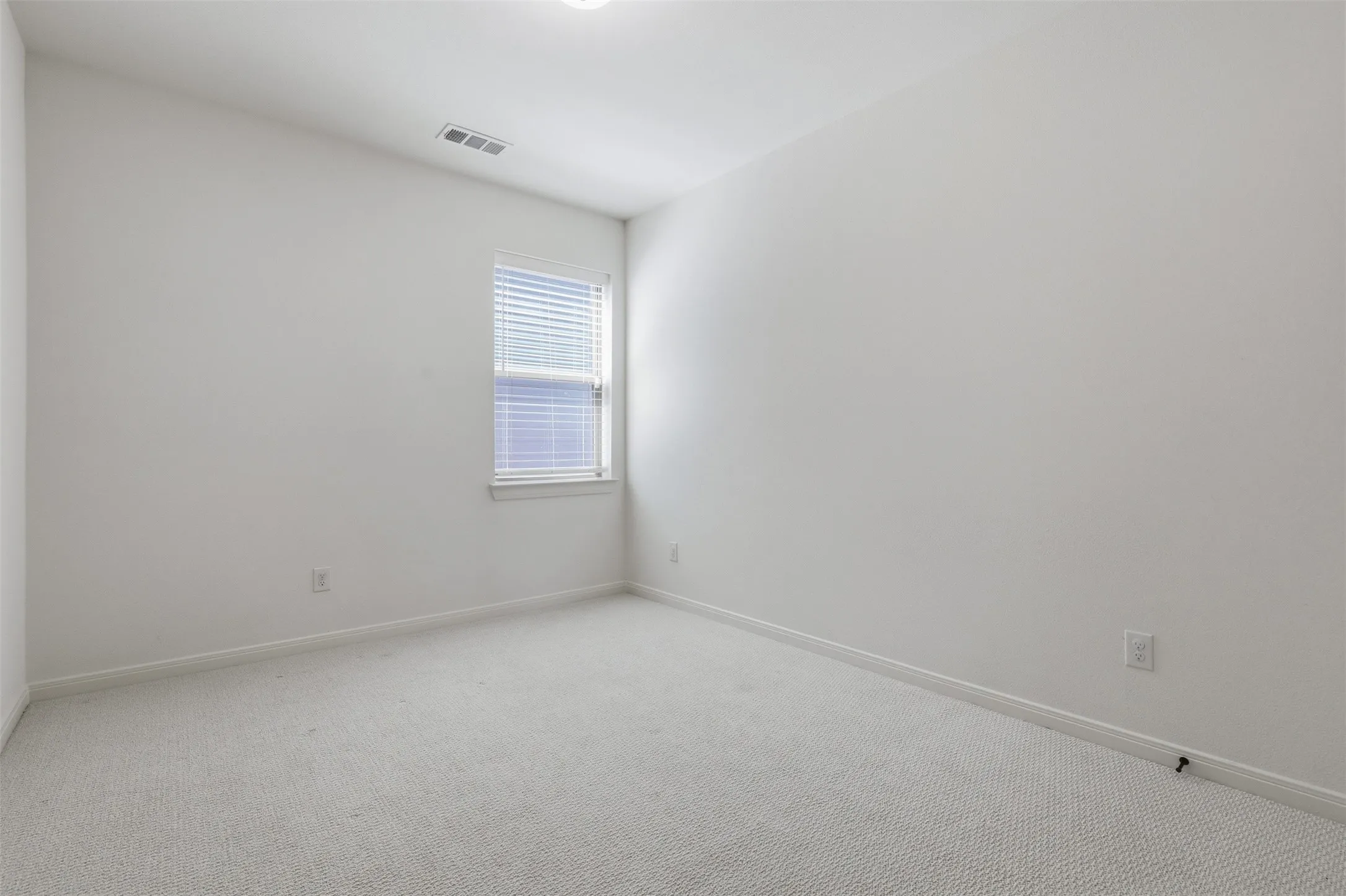 Carpeted interior space featuring white walls, a single window with blinds, and recessed lighting