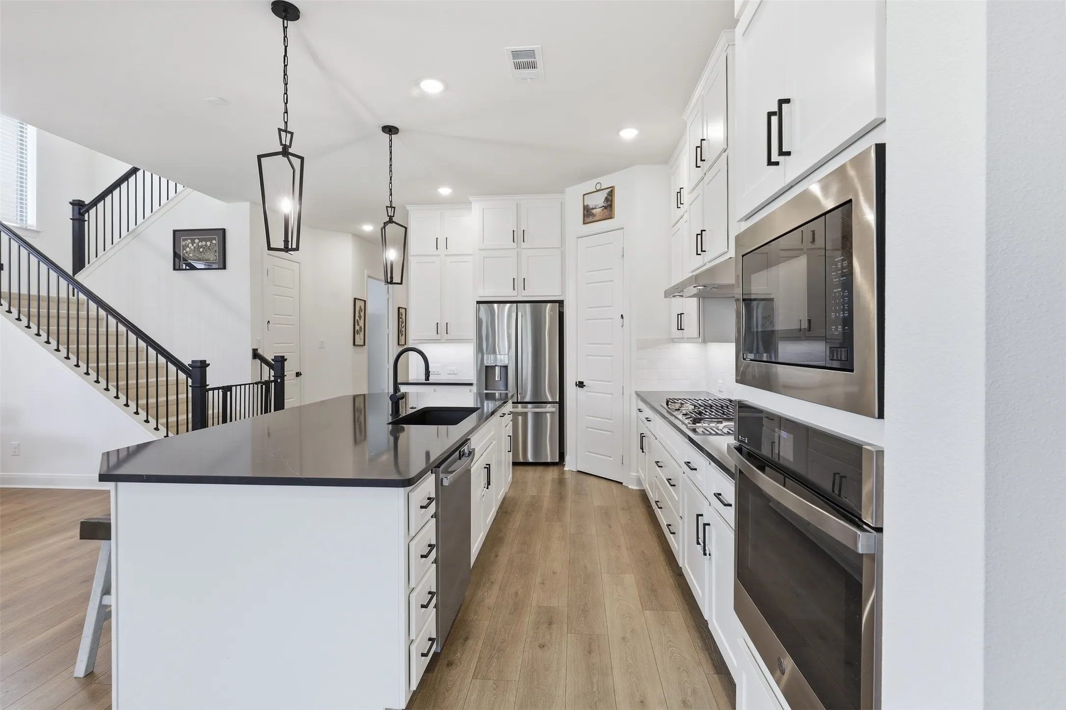 Modern kitchen featuring a large center island with dark countertop, white cabinetry with dark hardware, stainless steel appliances, and wood-finish flooring