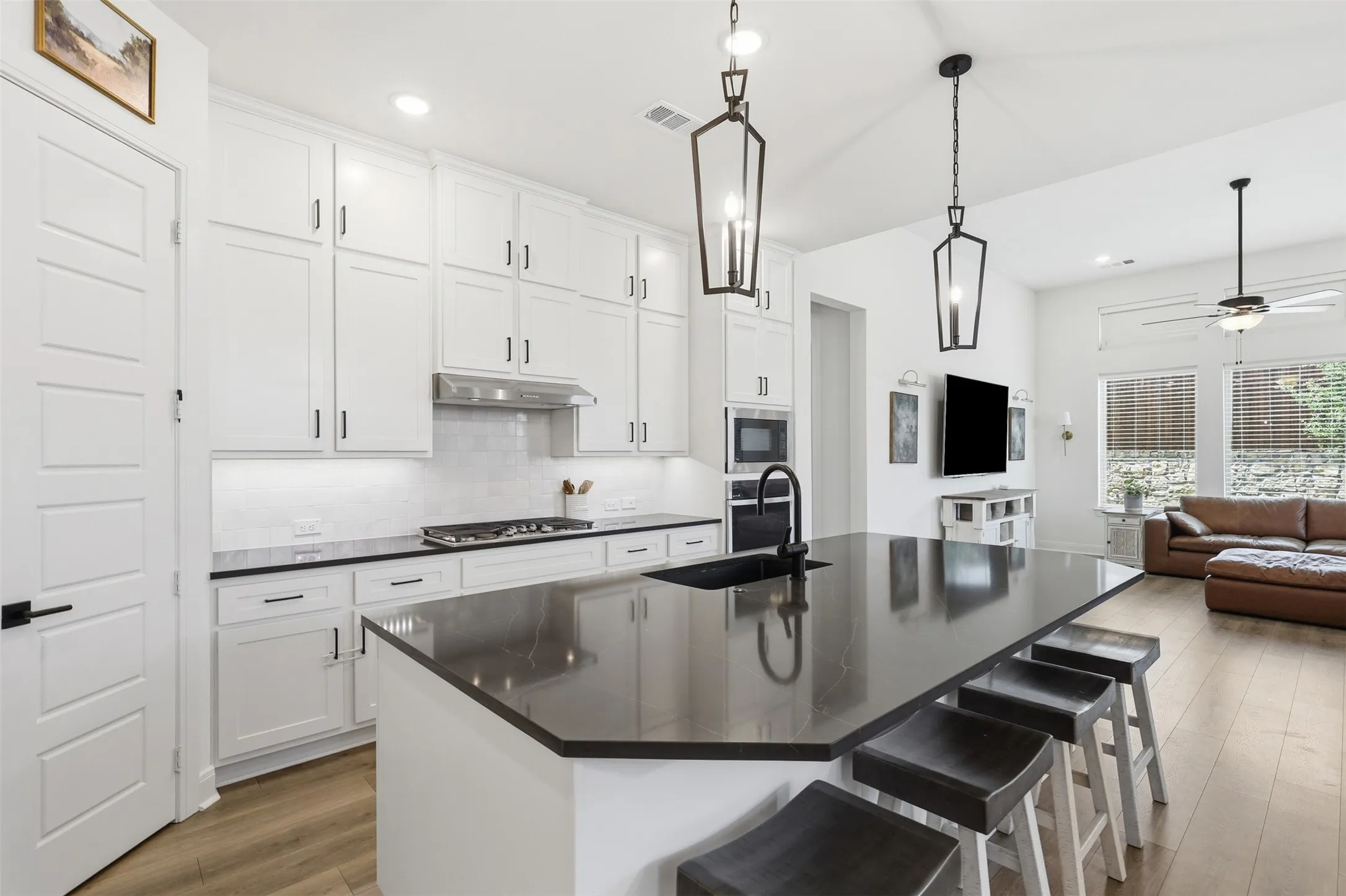Open-concept kitchen featuring an island with seating, white shaker cabinetry, stainless steel appliances, and wood-finish flooring