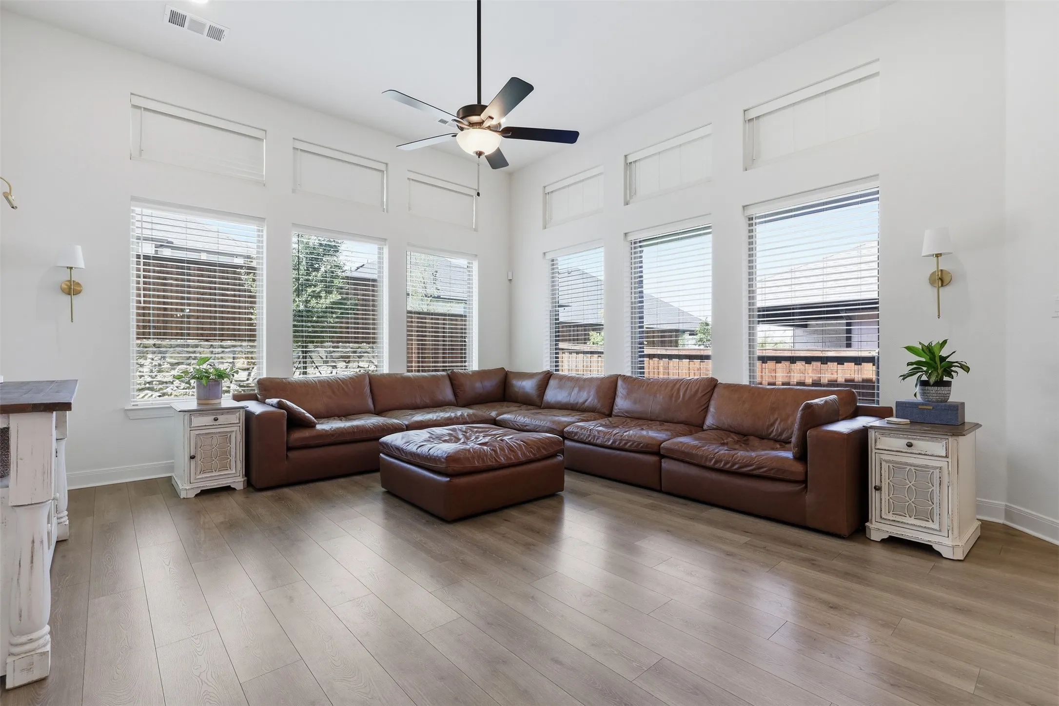 Spacious living area featuring high ceilings, extensive window arrays, wood-finish flooring, and a ceiling fan