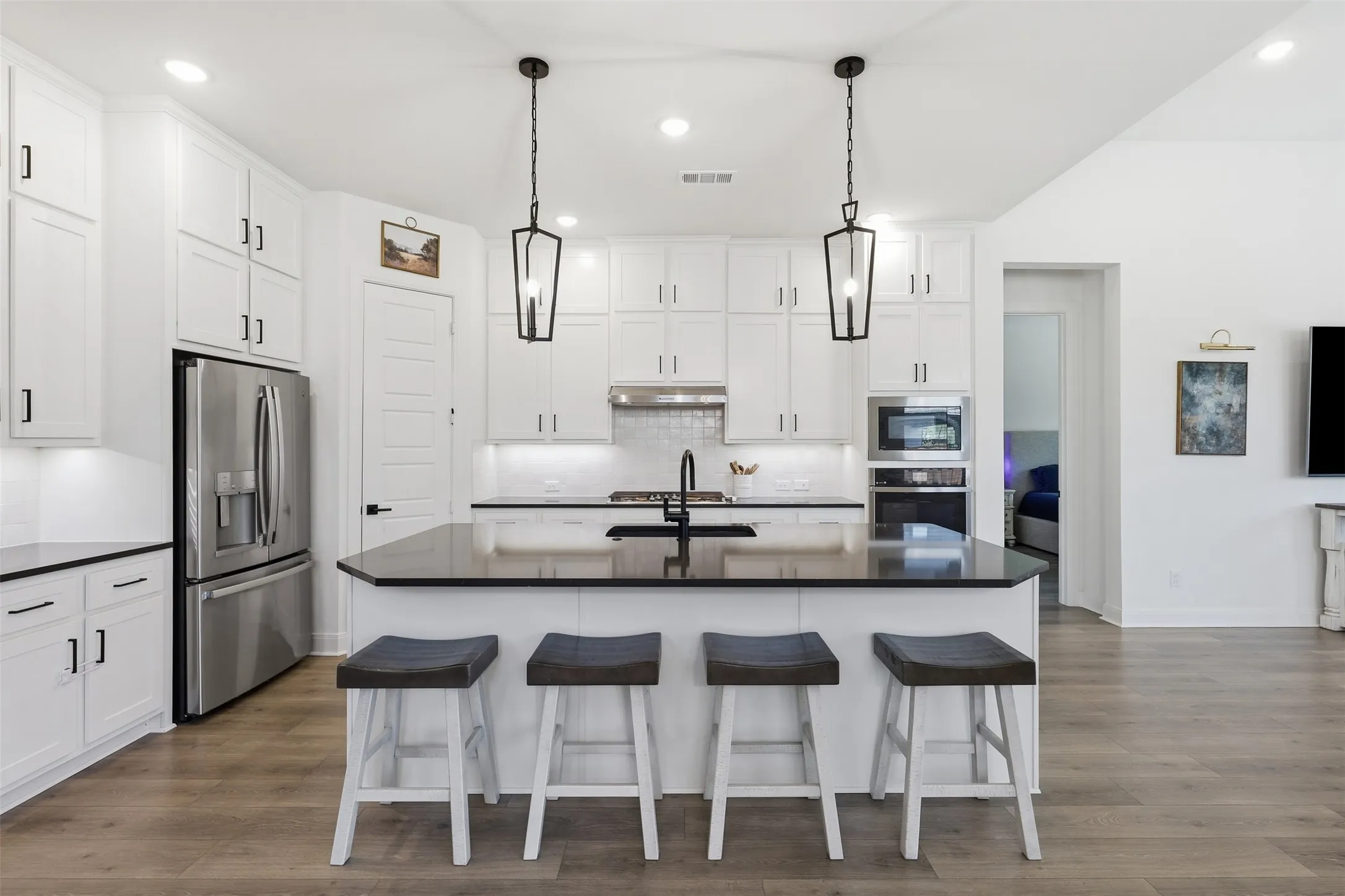 Bright kitchen featuring white shaker cabinetry, stainless steel appliances, a center island with bar seating, and wood-finish flooring