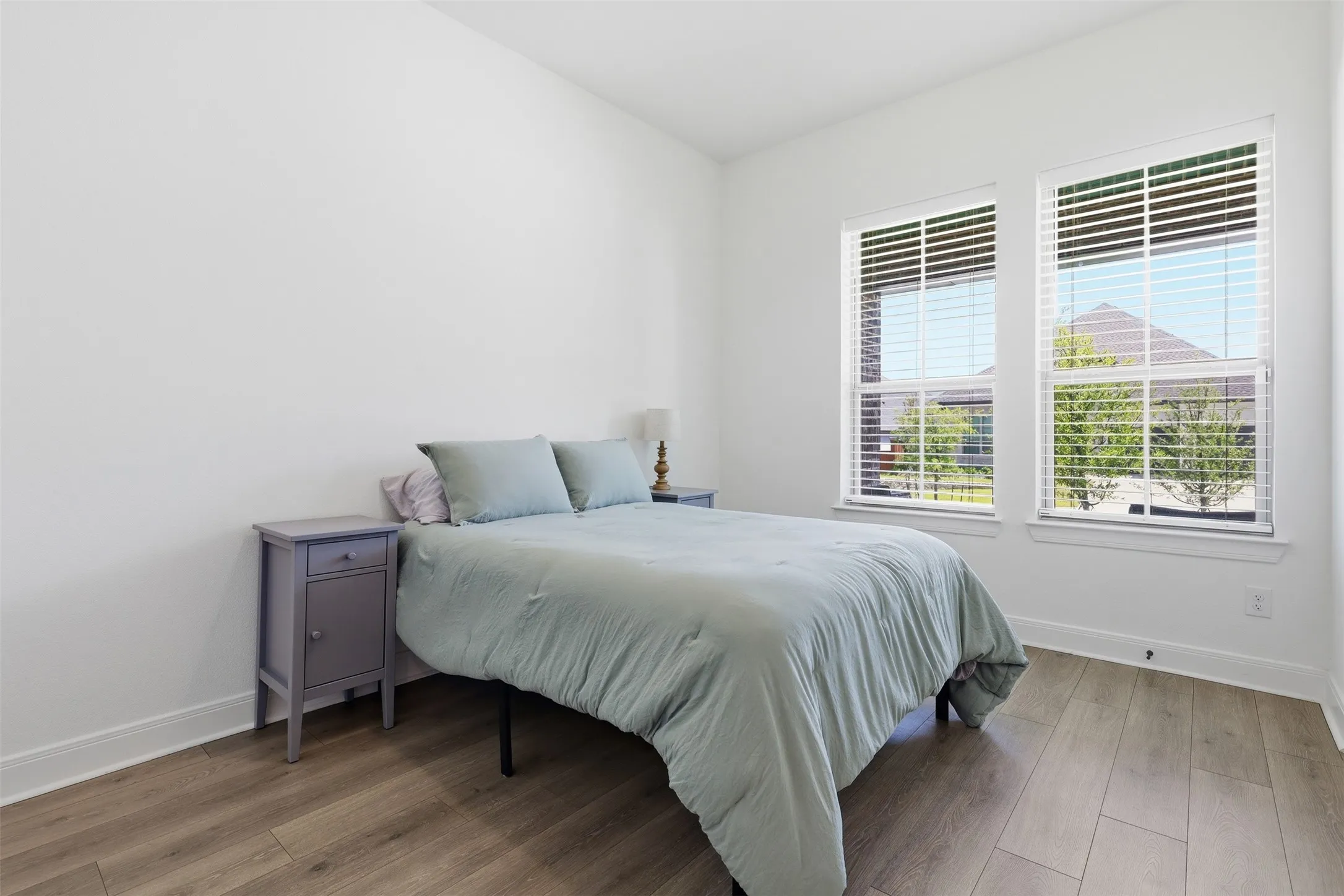Bright interior featuring two large windows with horizontal blinds, wood-finish flooring, white baseboards, and neutral wall tones