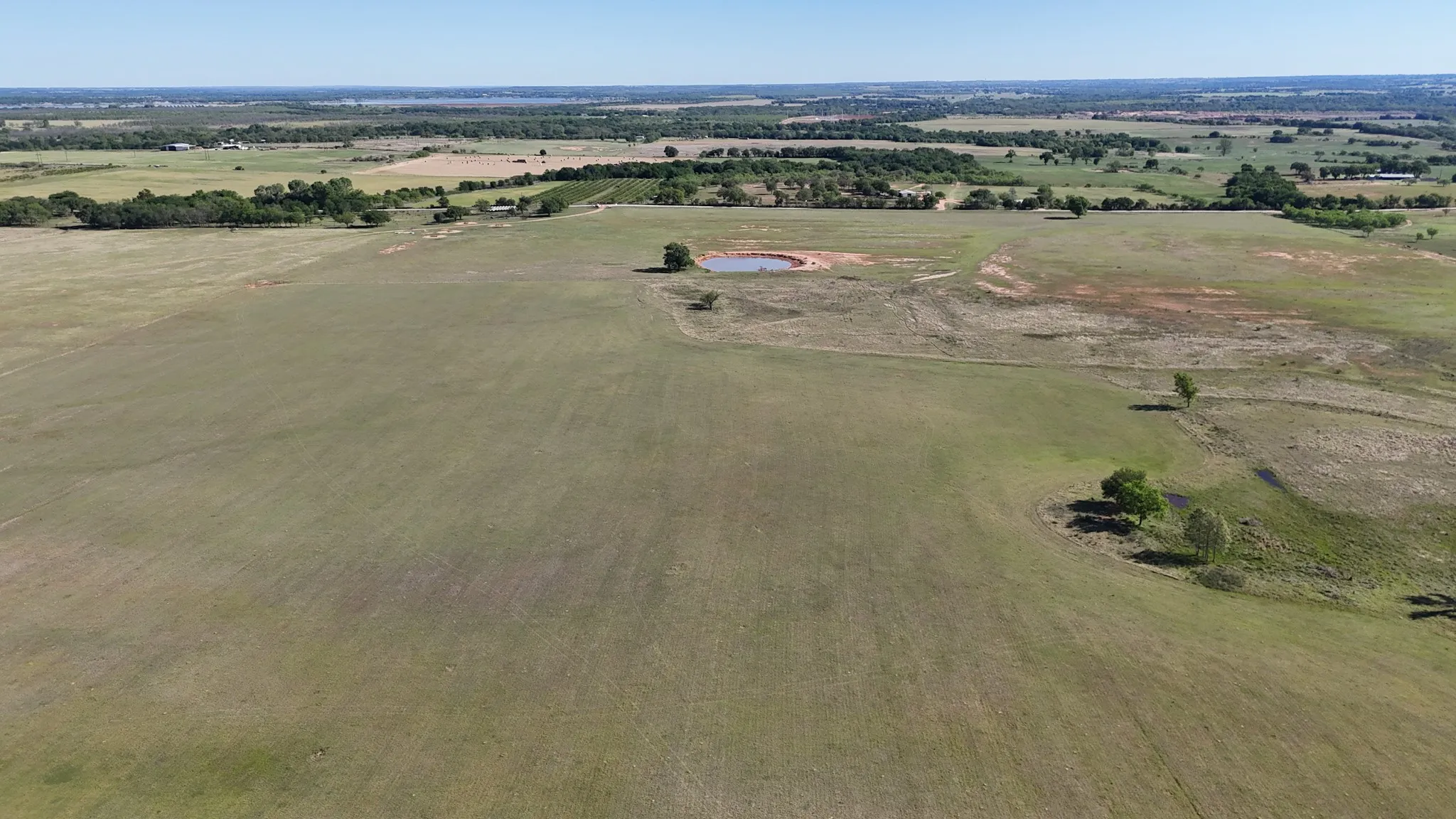 Expansive undeveloped acreage featuring a natural pond, scattered mature trees, and varied terrain
