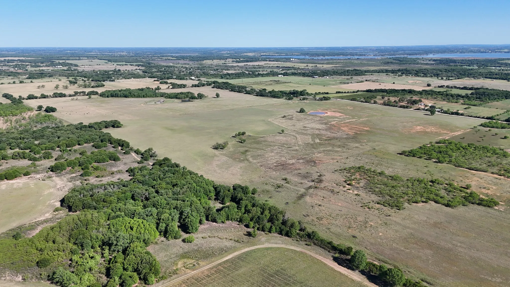 Expansive rural landscape featuring open fields, scattered tree lines, and a distant body of water