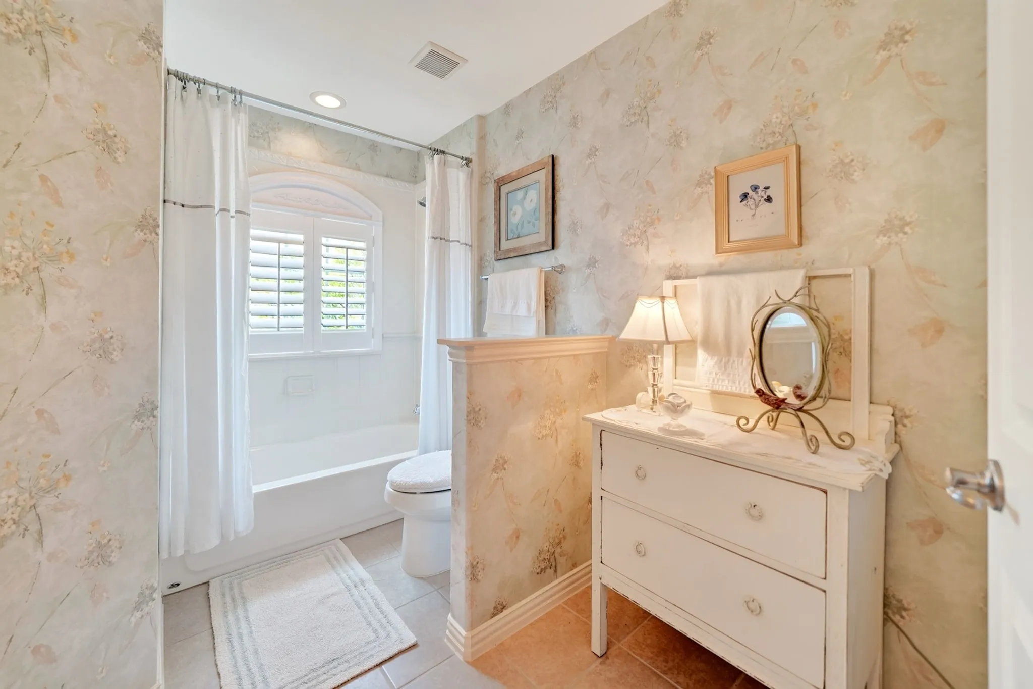 Bathroom featuring a bathtub with an arched window, white louvered shutters, and a shower curtain