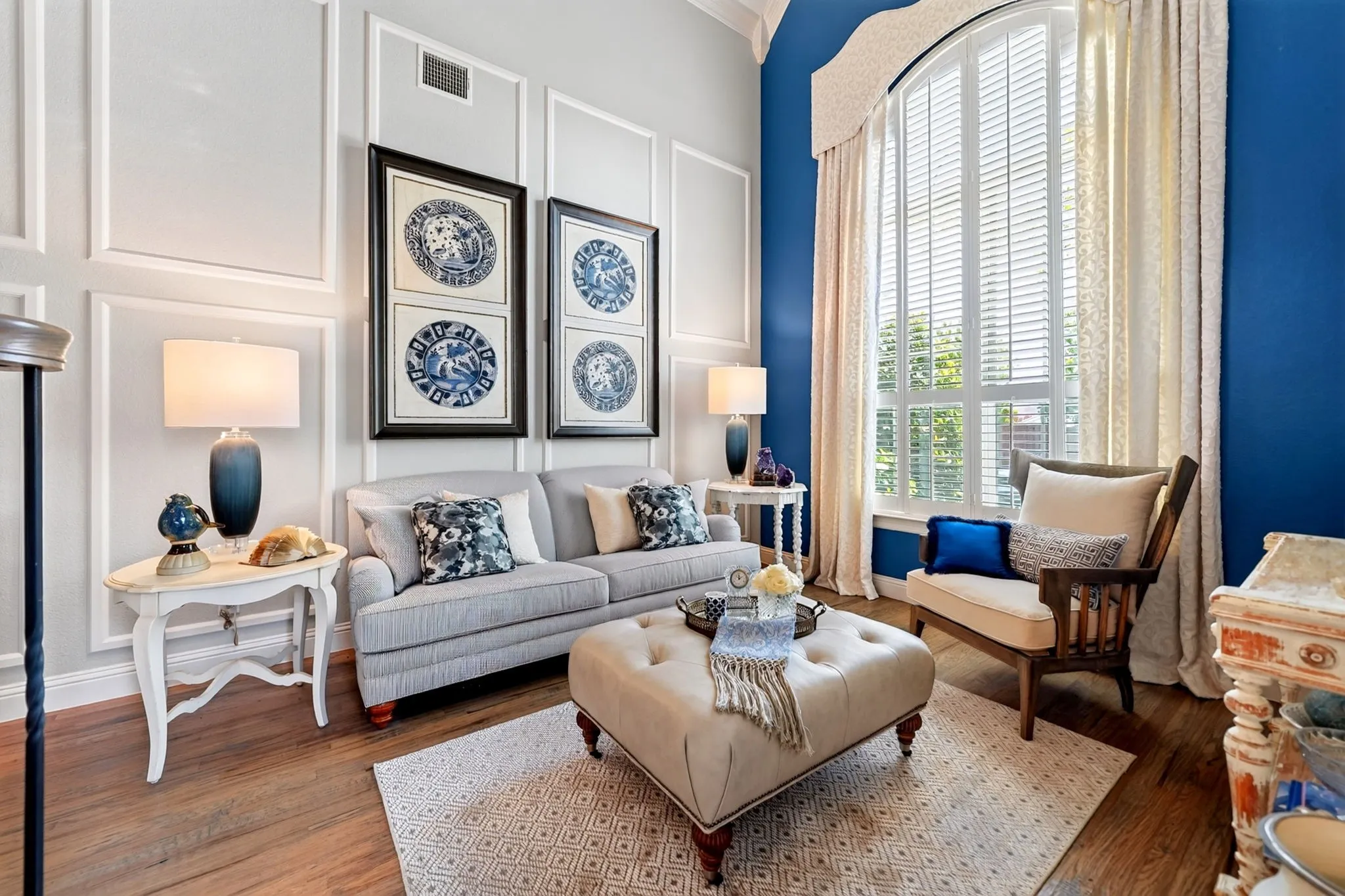 Living area featuring high ceilings, decorative wall molding, wood-finish flooring, and a large arched window with plantation shutters