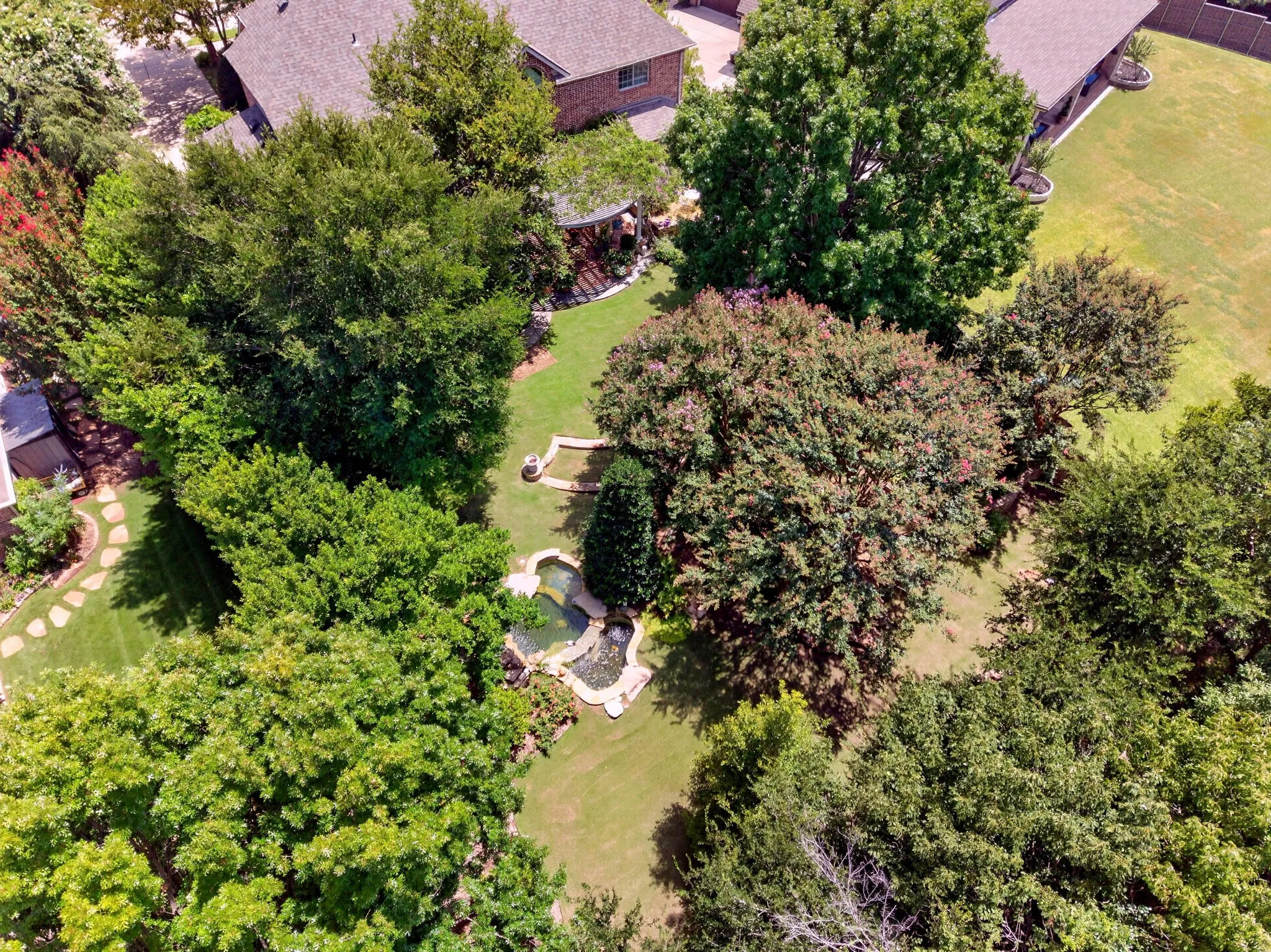 Spacious backyard with mature trees, manicured lawn, and stone-lined water features