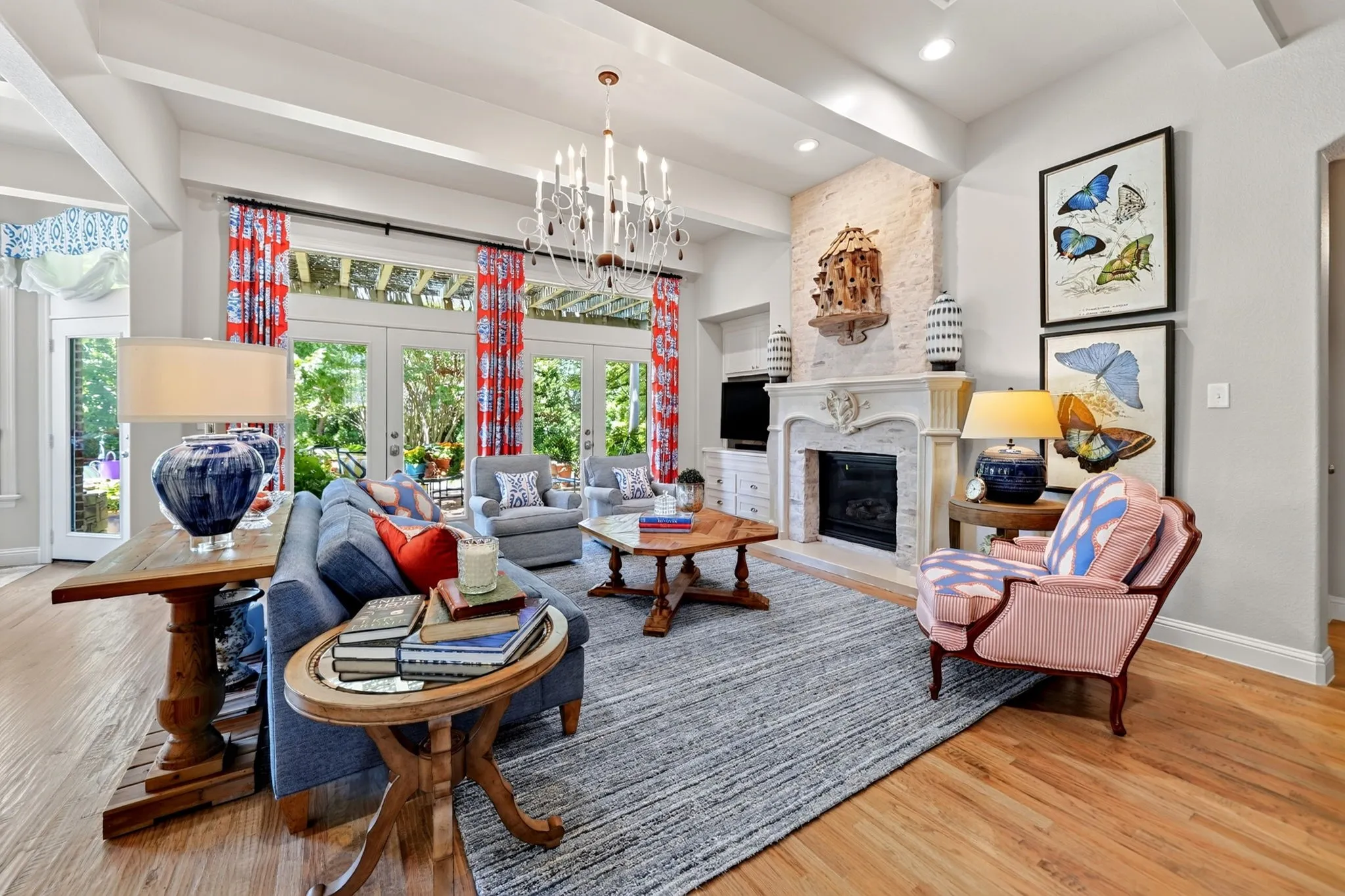 Spacious living area featuring wood-finish flooring, a white mantel fireplace with a light-colored stone surround, multiple French doors, and beamed ceilings