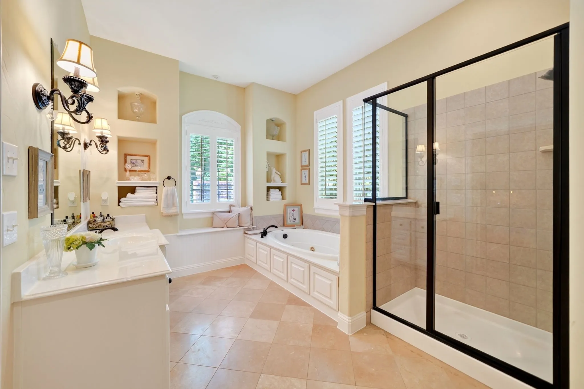 Neutral-toned bathroom featuring a spacious corner shower with glass enclosure, a built-in soaking tub with paneled surround, and a vanity with a light-toned countertop
