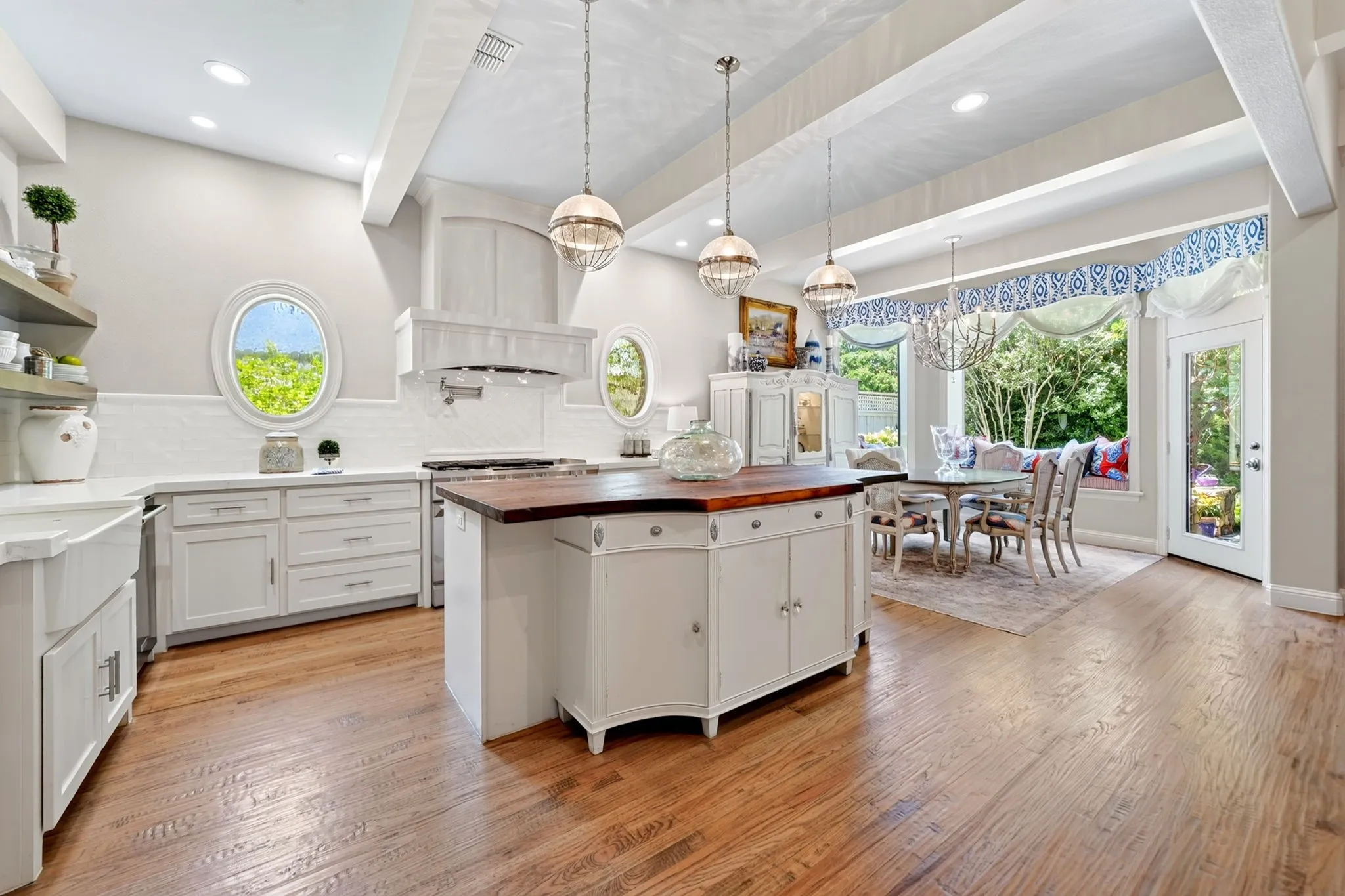 Spacious kitchen featuring hardwood flooring, a central island with butcher block countertop, white cabinetry with integrated appliances, white subway tile backsplash, and oval windows