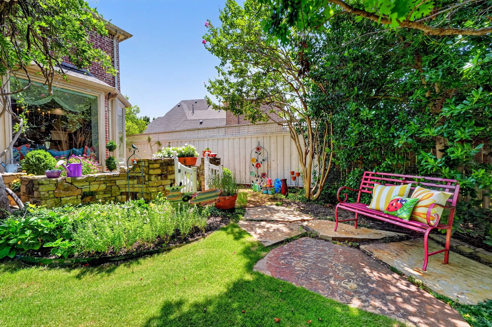 Manicured backyard featuring a stone retaining wall, mature trees, and a flagstone pathway