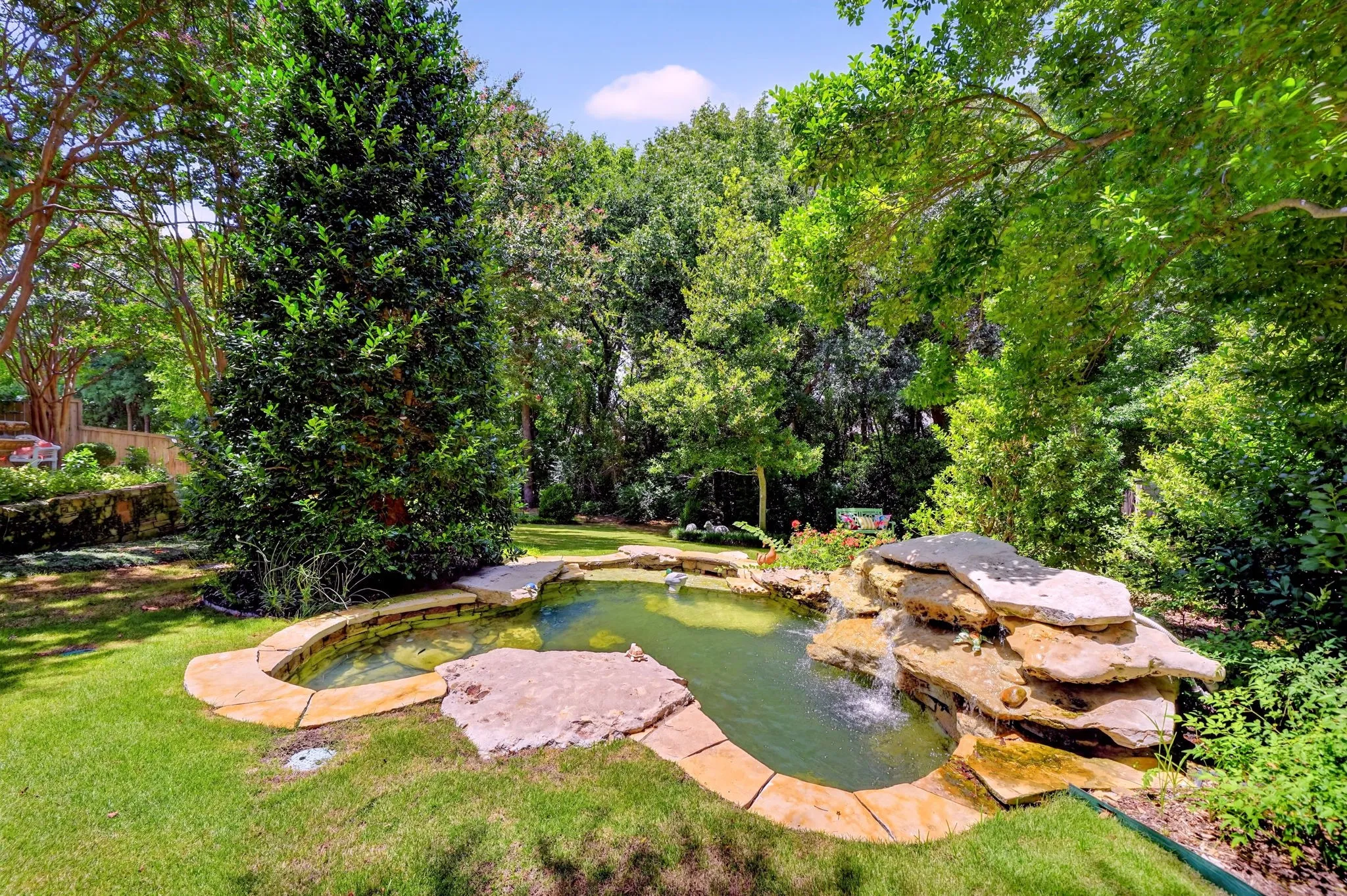 Manicured backyard oasis featuring a stone-lined pond with an integrated rock waterfall