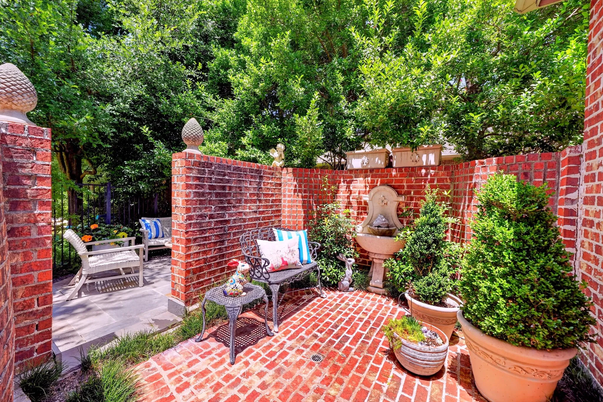 Brick paver patio featuring a wall-mounted water fountain, mature potted evergreens, and brick privacy walls with decorative finials